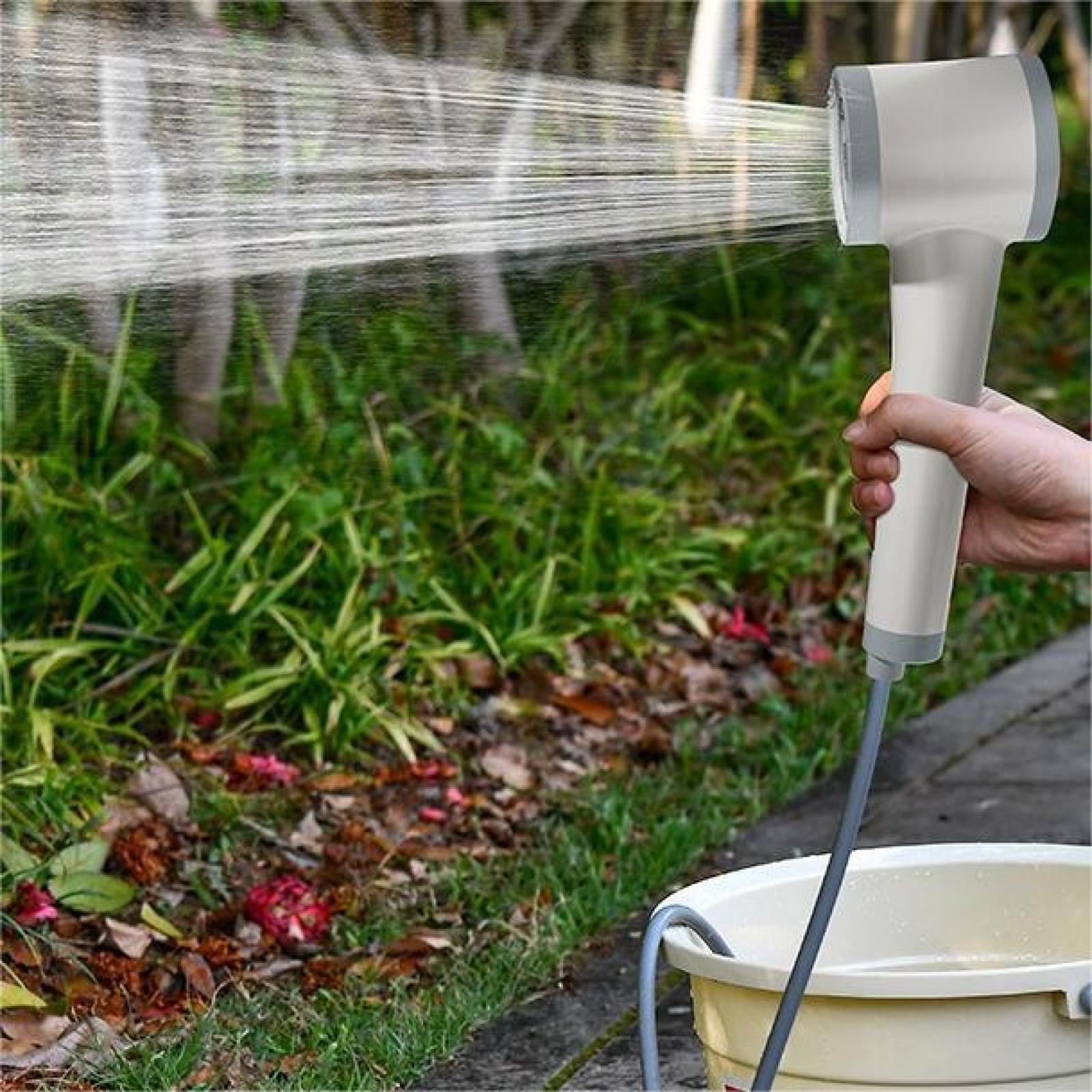 Eine Hand hält einen weißen und grauen Duschkopf und sprüht Wasser auf grünes Laub und einen Eimer.