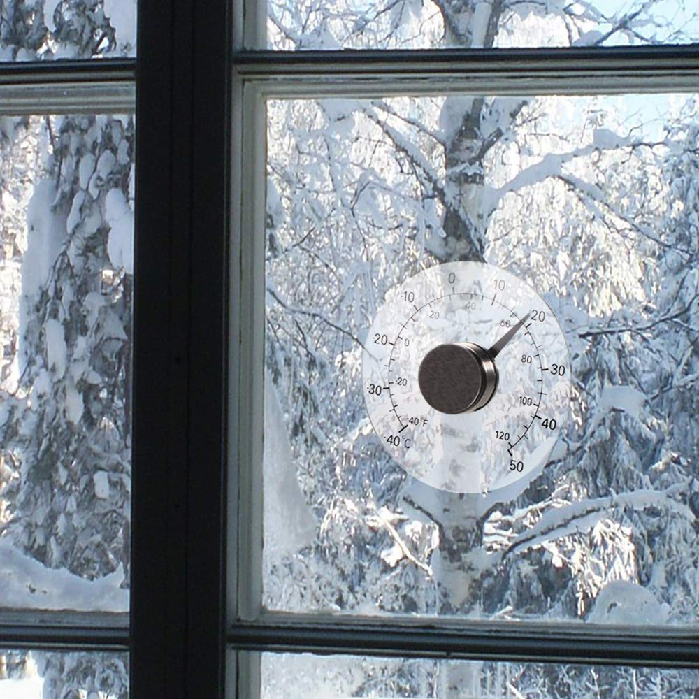 Ein Fenster zeigt eine verschneite Landschaft. Ein Thermometer ist am Glas befestigt. Es zeigt eine sehr kalte Temperatur an.