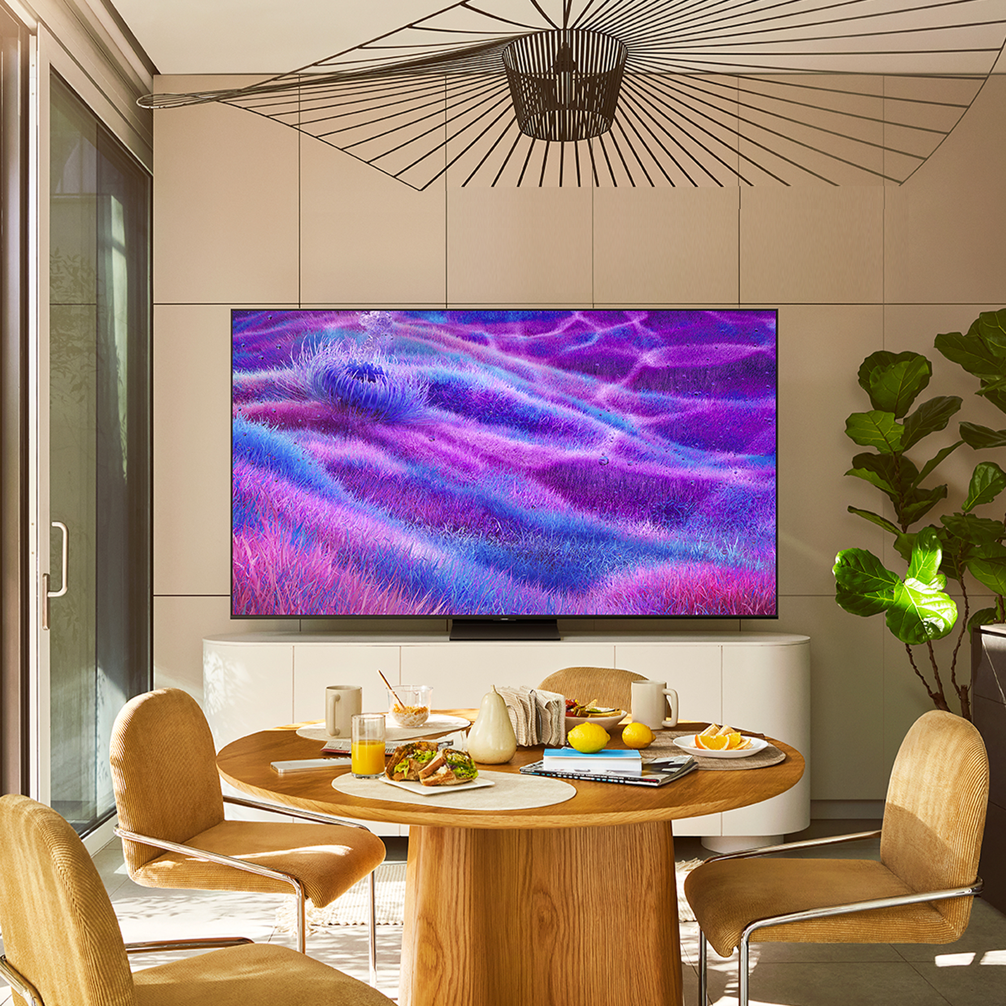 Salle à manger avec TV affichant art violet, table ronde pour repas et chaises jaunes. Lumière naturelle inonde la pièce.