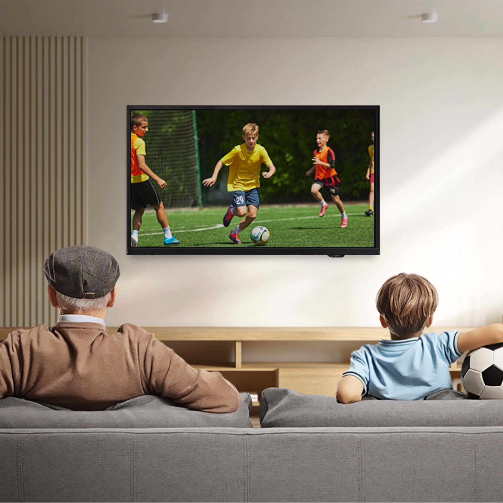 Telewizor pokazuje mecz piłki nożnej. Starszy mężczyzna i chłopiec siedzą na kanapie i oglądają mecz. W pobliżu jest piłka nożna.