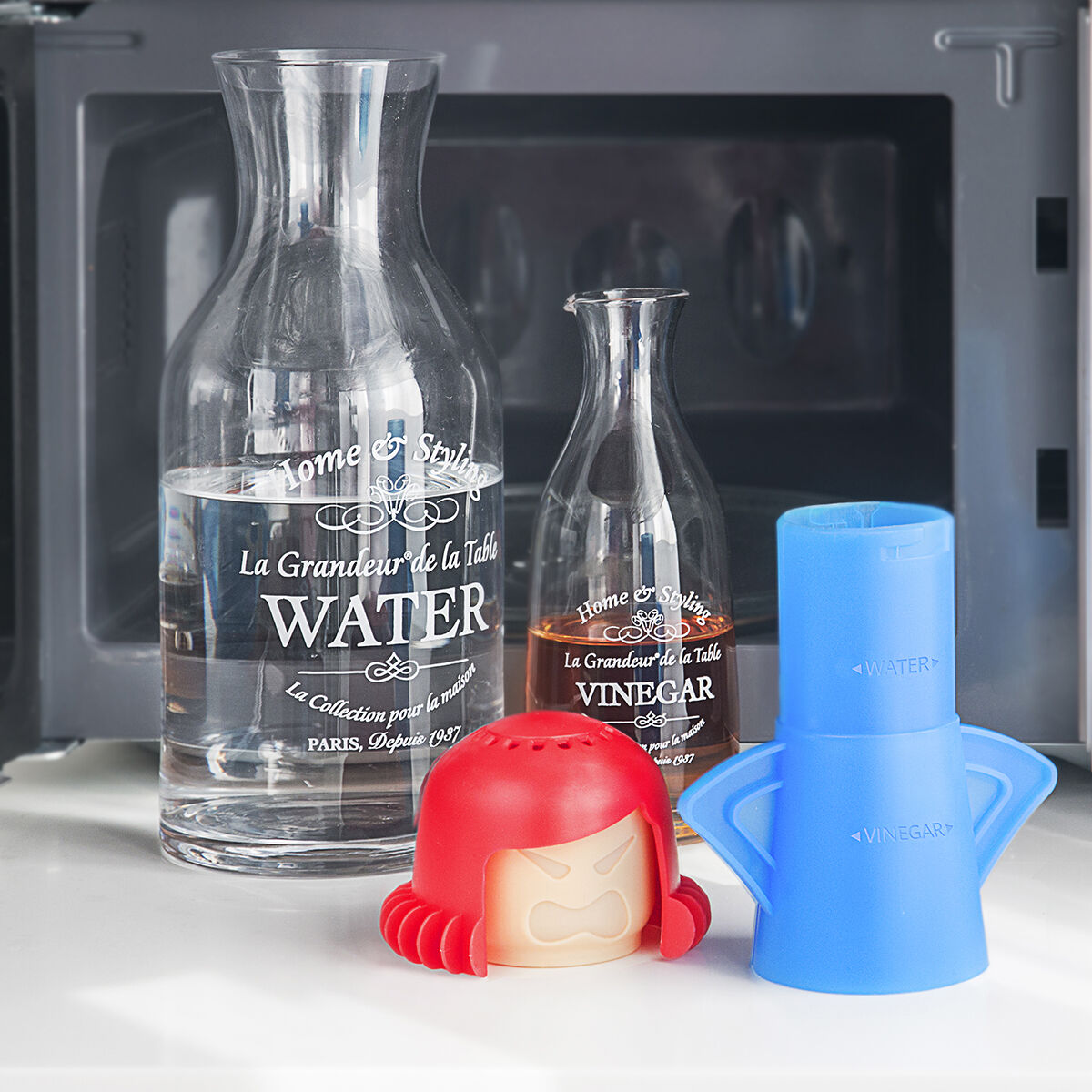 Bottiglie di vetro con acqua e aceto, un contenitore rosso e uno blu, davanti a un microonde.
