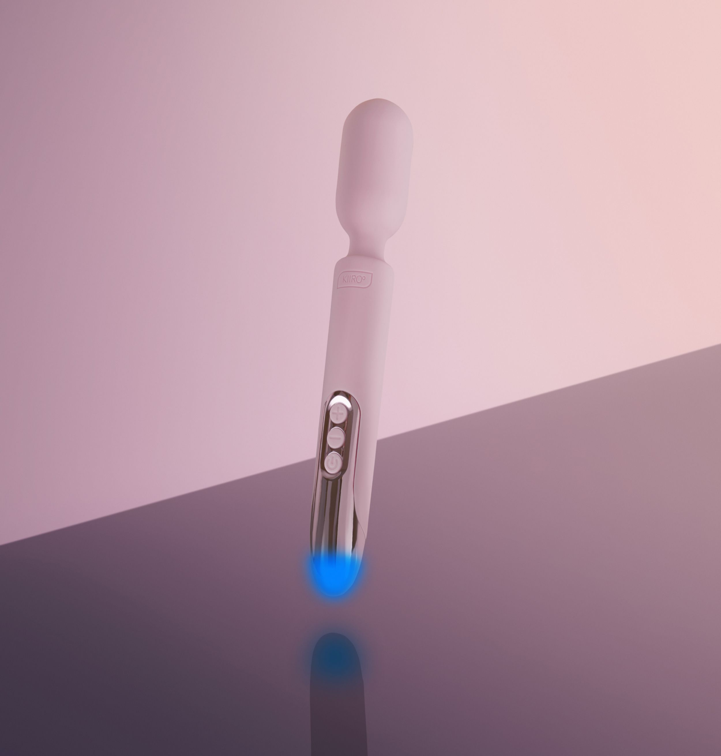 Ein rosa KIIRO-Zauberstab mit silbernen Bedienelementen und einer blau leuchtenden Basis. Es befindet sich auf einer reflektierenden Oberfläche.