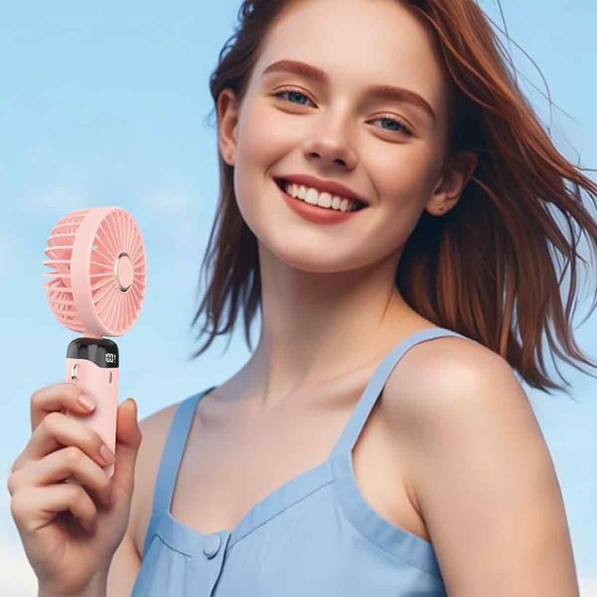 Eine lächelnde Frau hält einen rosa Ventilator. Sie trägt ein blaues Oberteil. Der Hintergrund ist ein klarer blauer Himmel.