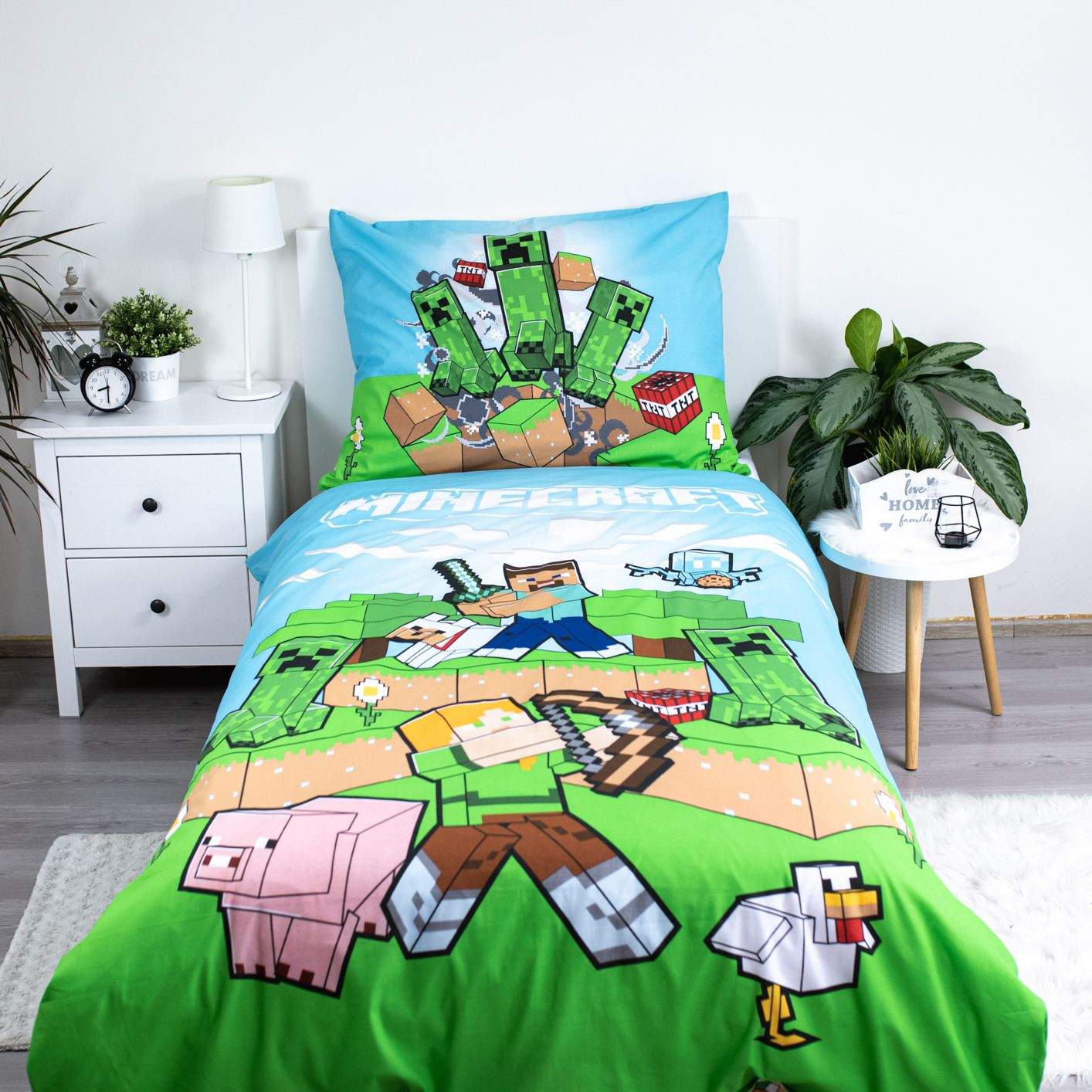 Minecraft-Bettwäsche mit Creeper-, Steve-, Schweine- und Hühnerfiguren. Grünes Gras, blauer Himmel und weiße Möbel im Hintergrund.