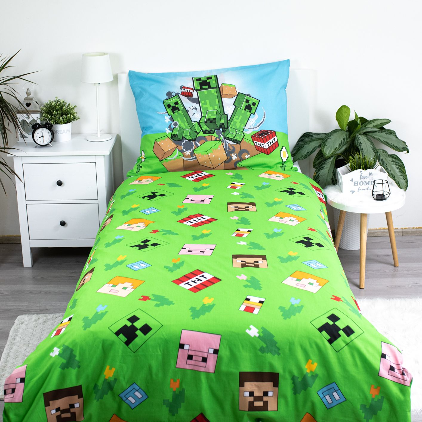 Ein Bettwäsche-Set zum Thema Minecraft. Grüne Bettdecke mit Charaktermustern. Kissen mit Creeper-Charakteren. Weißer Nachttisch und Pflanzen.