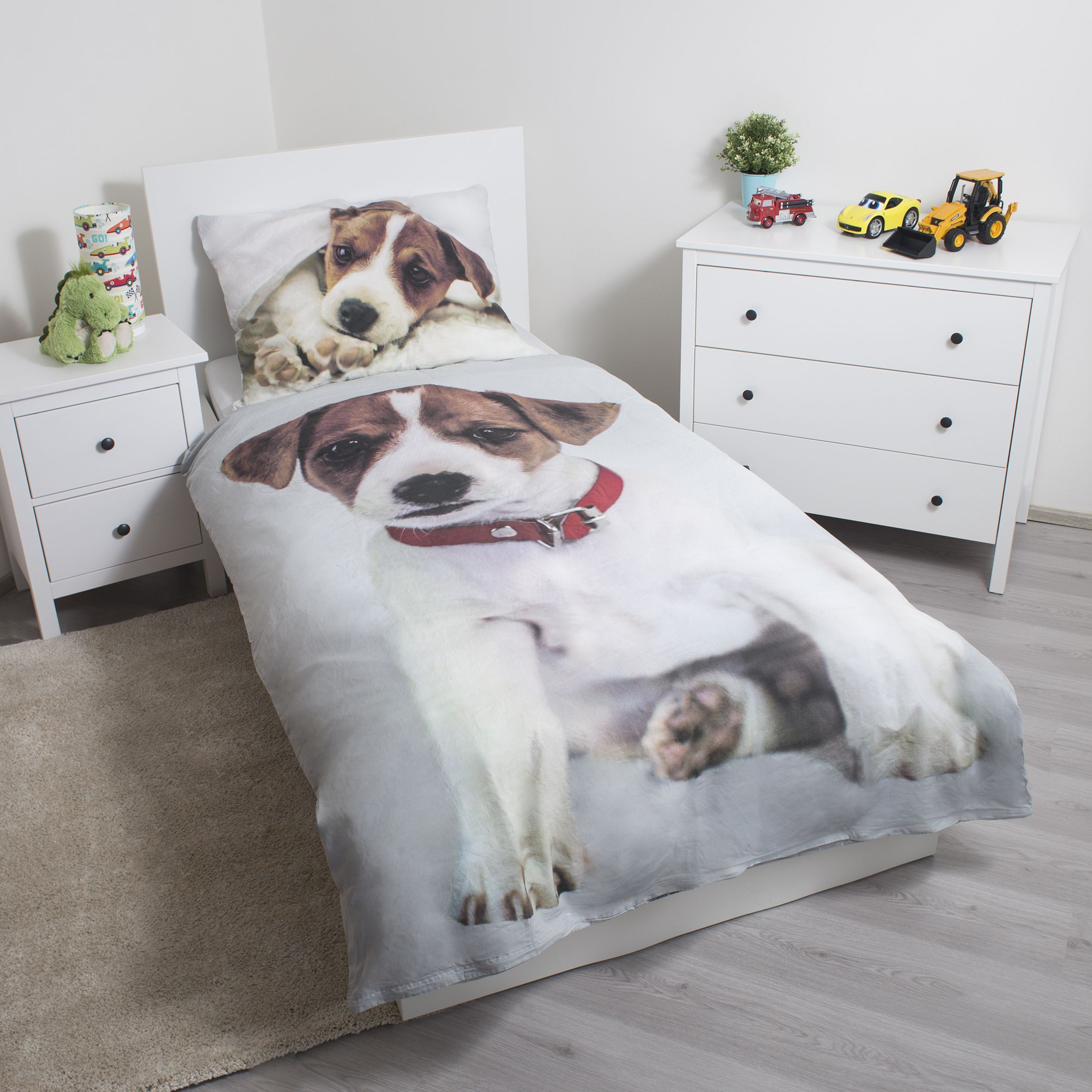 Schlafzimmer mit Hunde-Bettwäsche. Spielzeug und ein Nachttisch sind zu sehen. Die Bettwäsche zeigt einen Hund mit rotem Halsband.