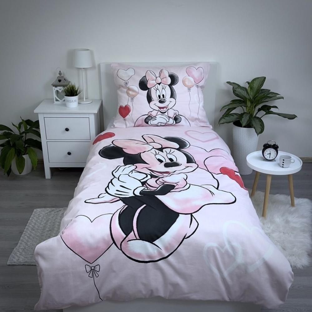 Ein rosa Minnie-Mouse-Bettwäsche-Set wird gezeigt. Minnie ist auf dem Kissen und der Bettdecke. Eine Pflanze, eine Uhr und eine Lampe sind ebenfalls sichtbar.