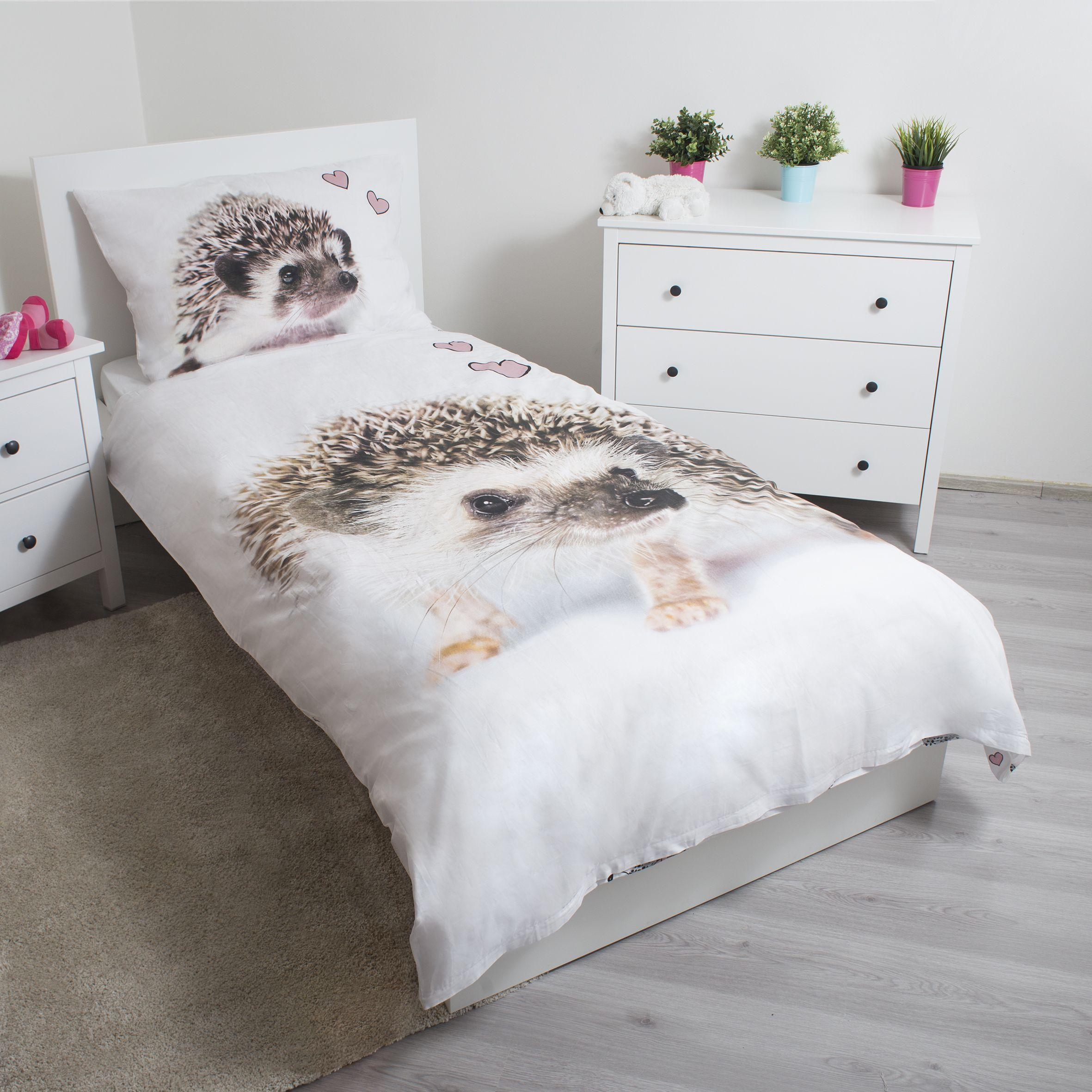 Ein Bett mit einem Igel-Design auf Bettdecke und Kissen. Eine weiße Kommode und ein Nachttisch sind im Raum zu sehen.