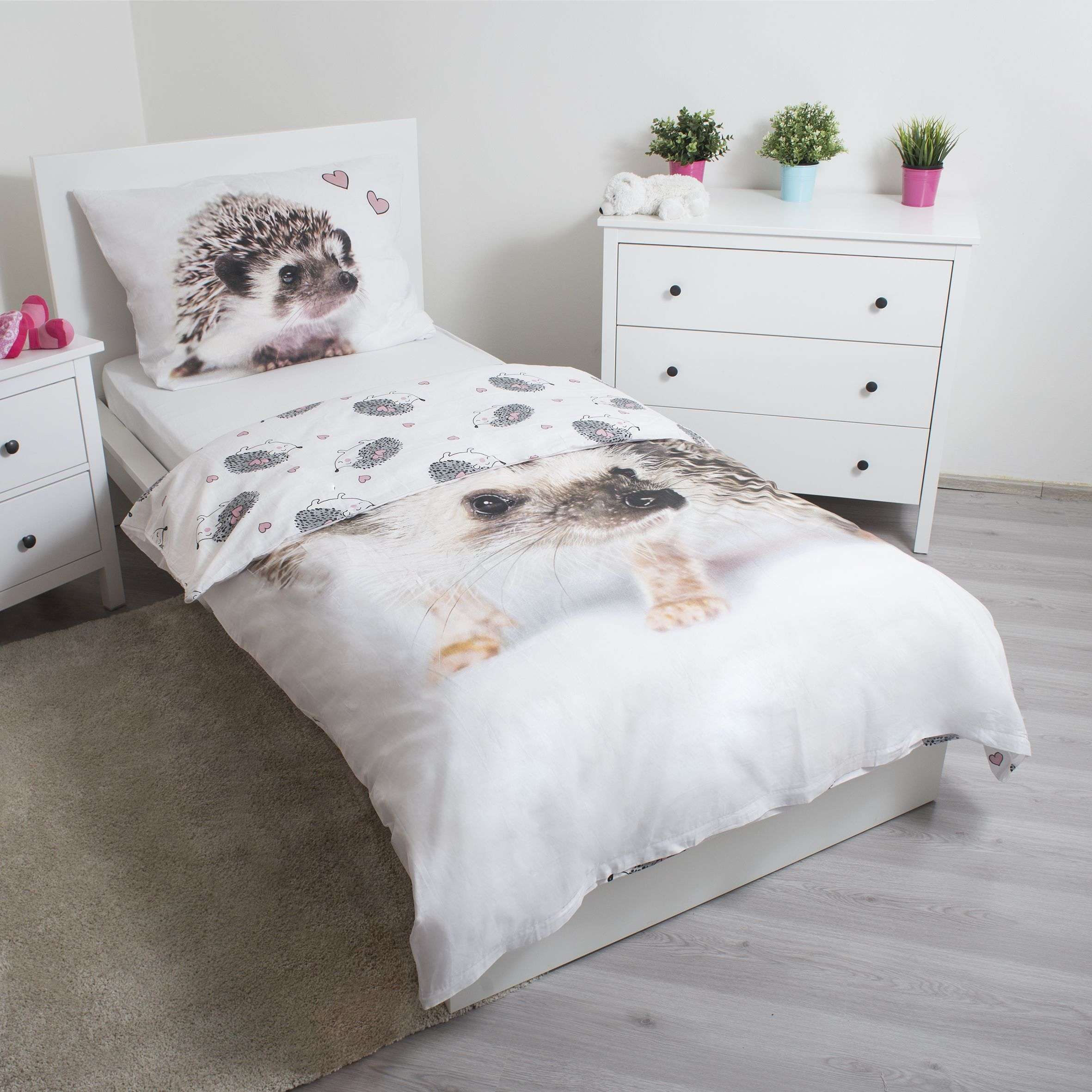 Ein Kinderzimmer mit Bett, Igelbettwäsche, Nachttisch, Kommode mit Pflanzen und einem Teppich.