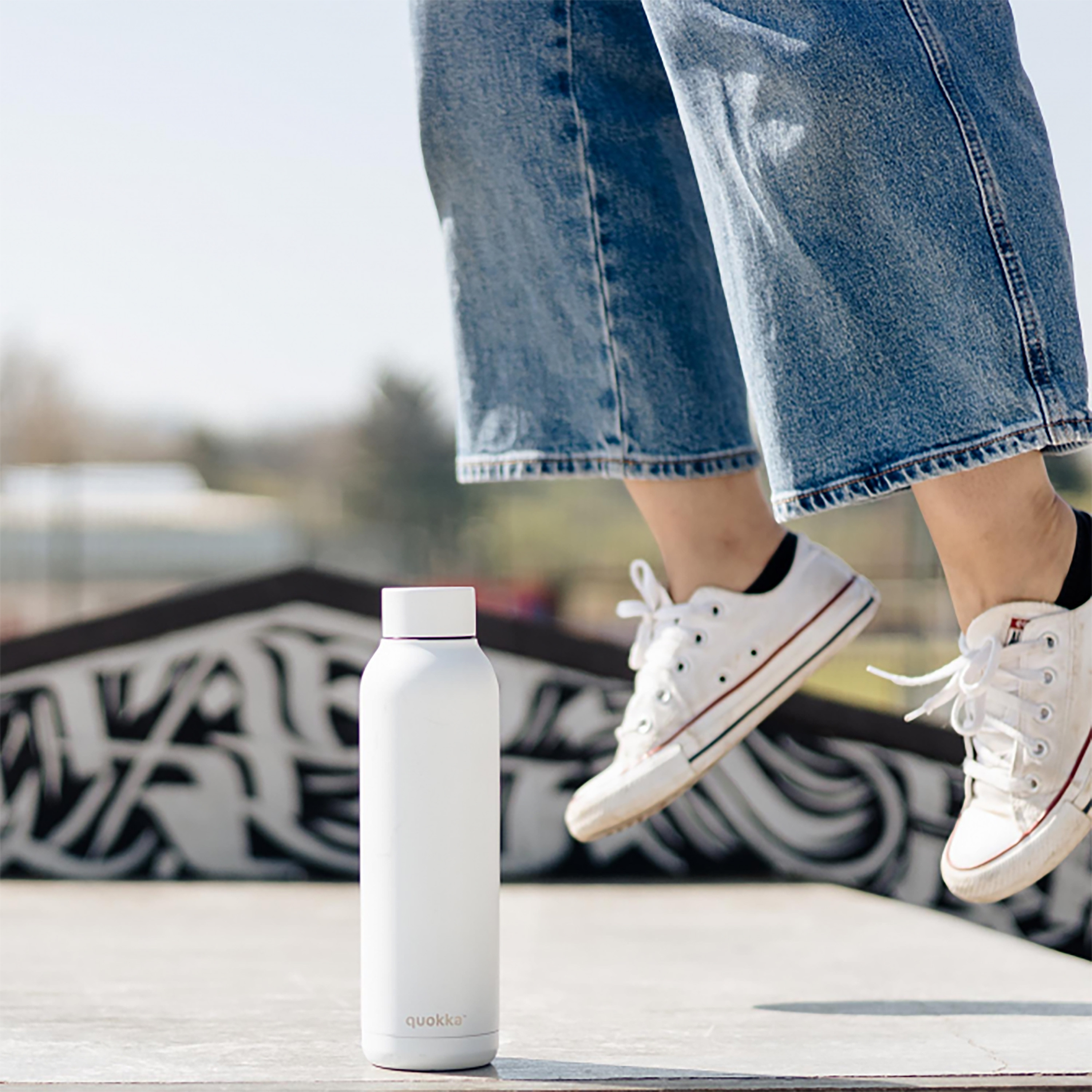 Bottiglia d'acqua bianca e gambe di una persona in jeans, scarpe da ginnastica bianche. Bottiglia in piedi, persona che salta.