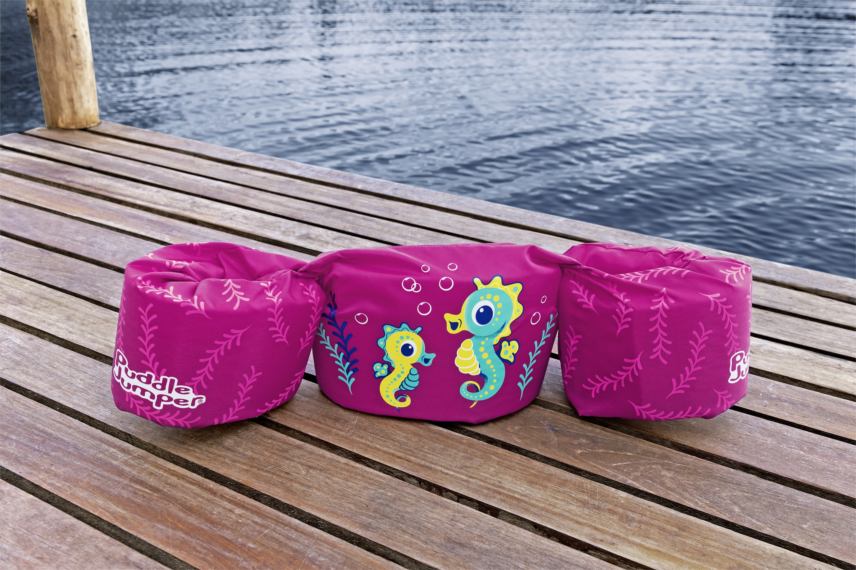 Galleggiante rosa Puddle Jumper su pontile di legno. Ha disegni di cavallucci marini ed è vicino all'acqua. Lo sfondo è sfocato.