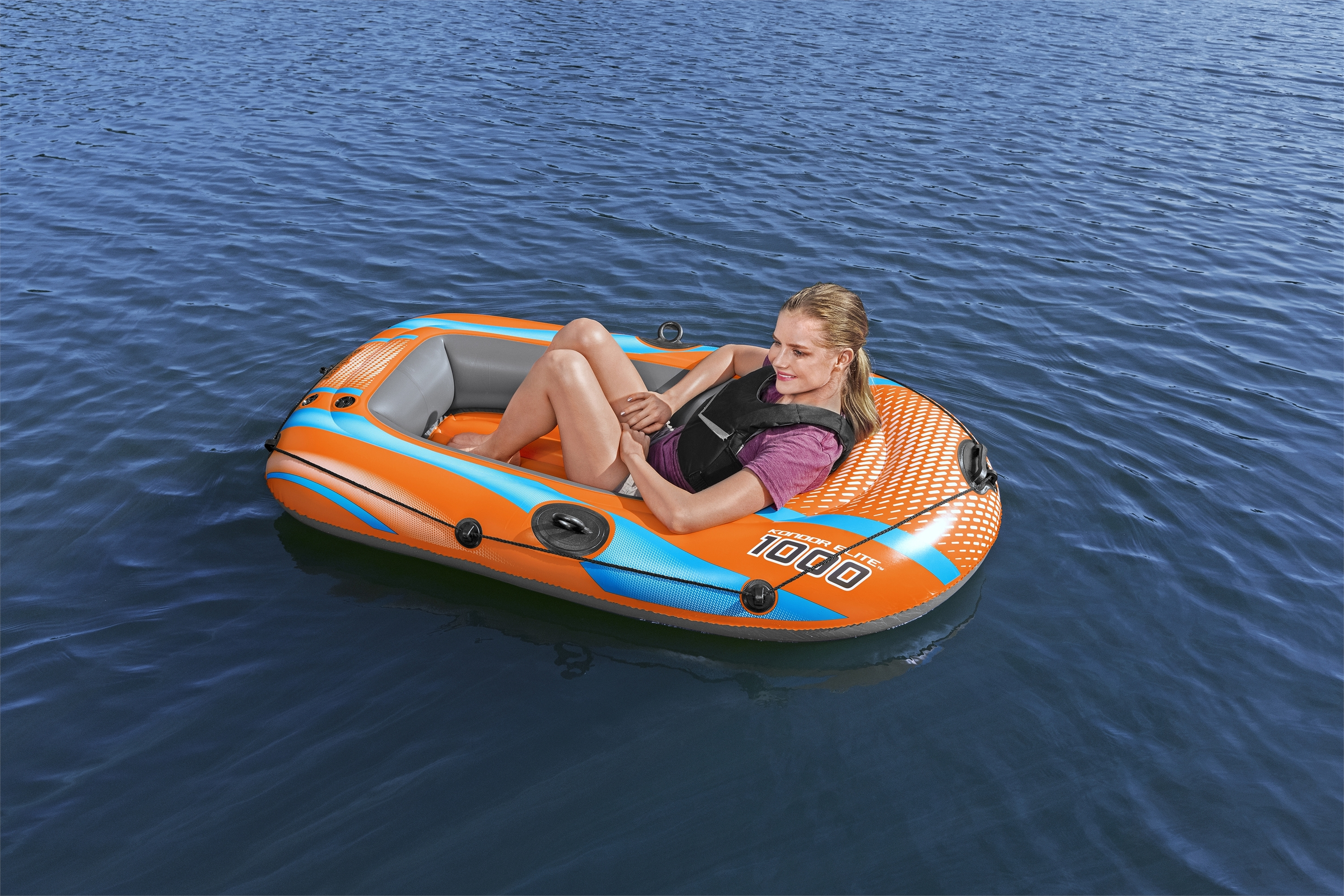 Eine Frau in einem orangefarbenen und blauen Schlauchboot auf dem Wasser. Sie trägt eine Schwimmweste und lächelt.