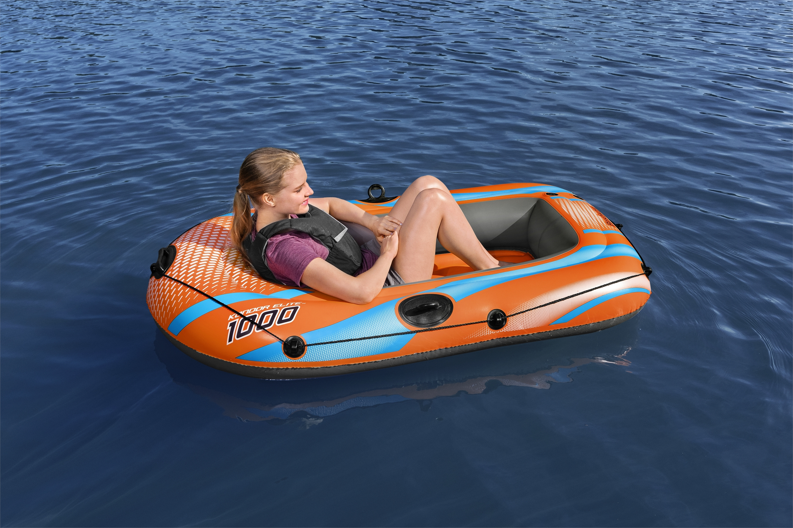 Eine Frau in einem orange-blauen Schlauchboot treibt auf blauem Wasser. Sie trägt eine Schwimmweste.
