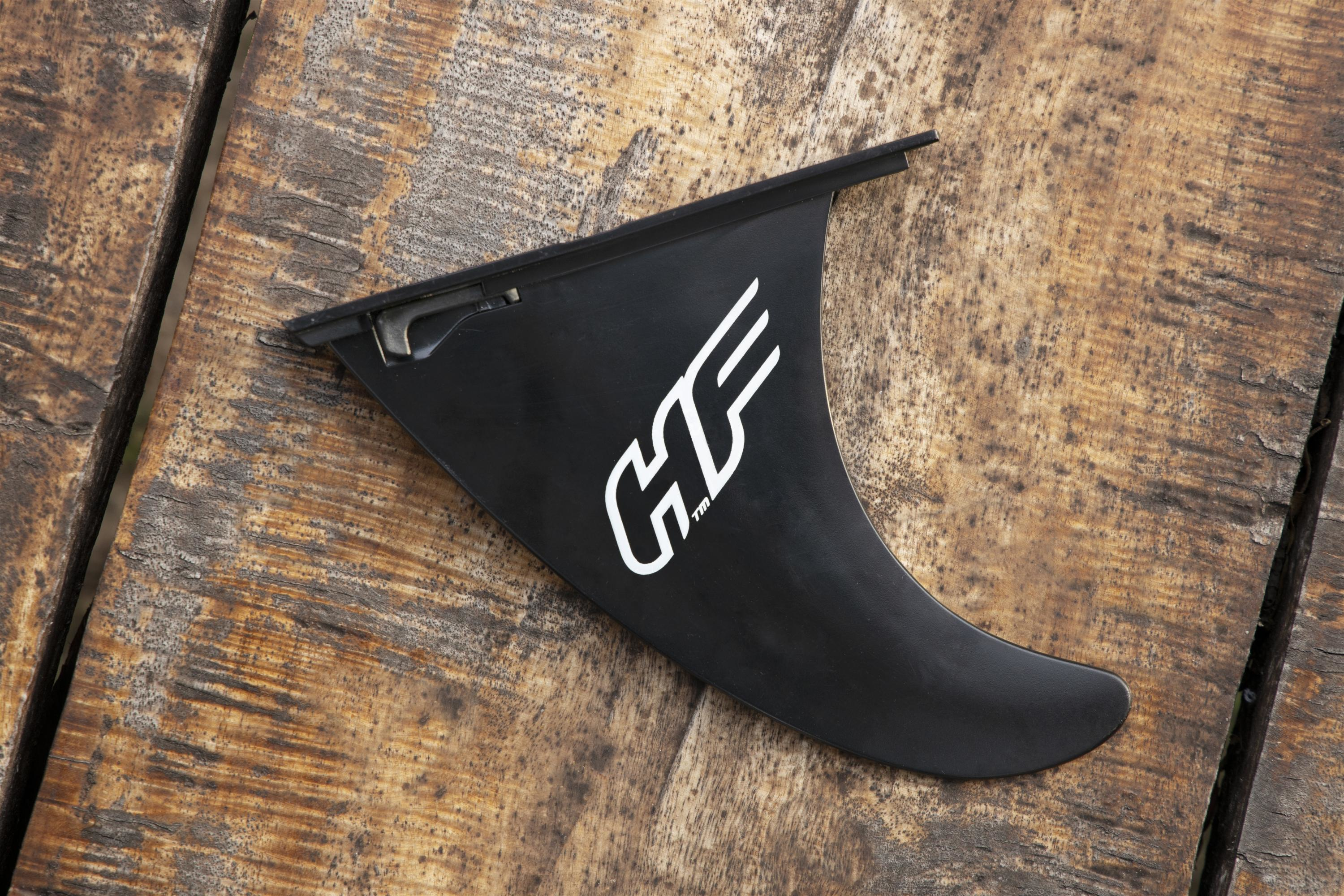 Een zwarte surfvinnen met een wit logo ligt op een verweerd houten oppervlak. Het logo zegt 'HF'.