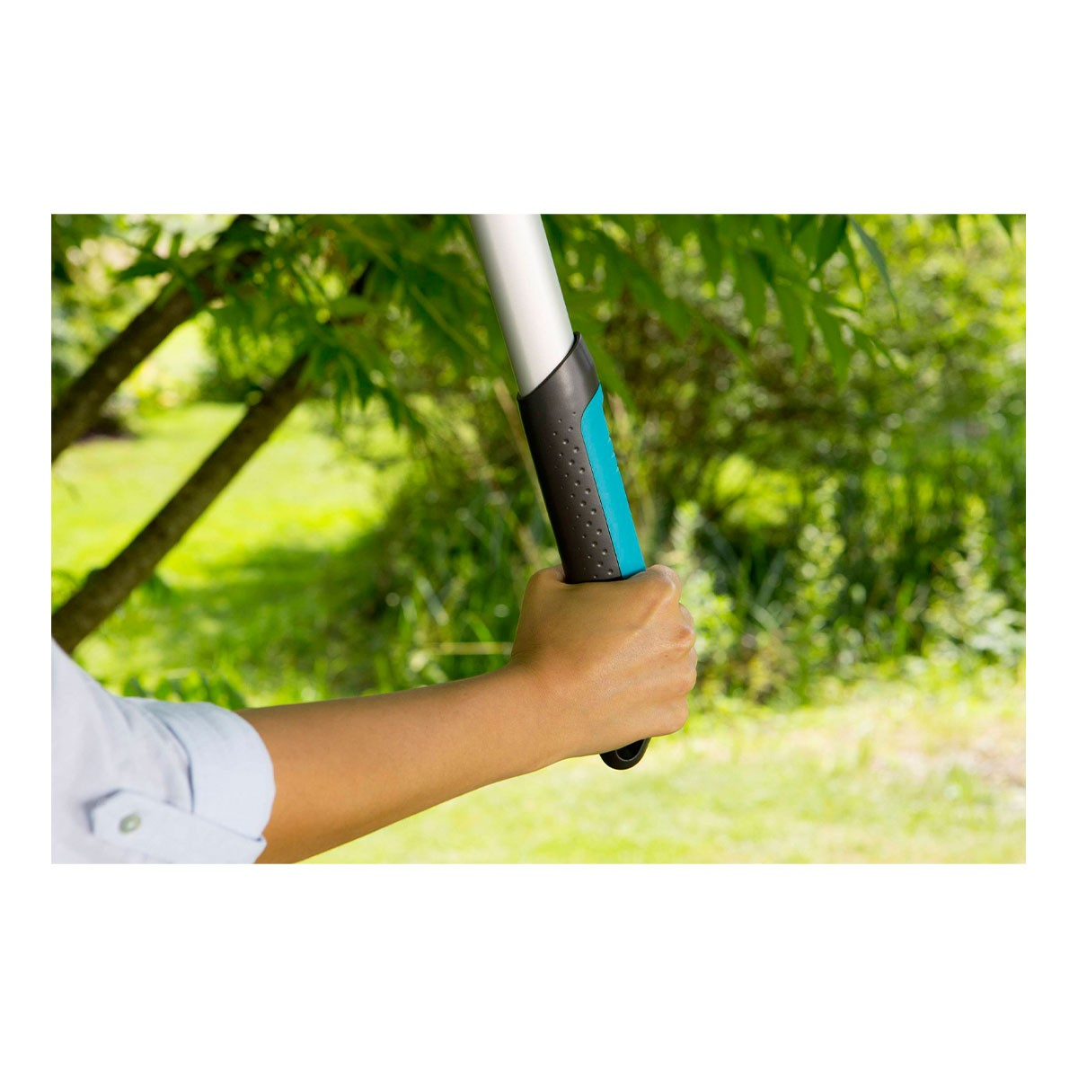 Una mano tiene in mano un attrezzo da giardinaggio. L'attrezzo ha un'impugnatura nera e turchese con un palo argentato. Fogliame verde sullo sfondo.