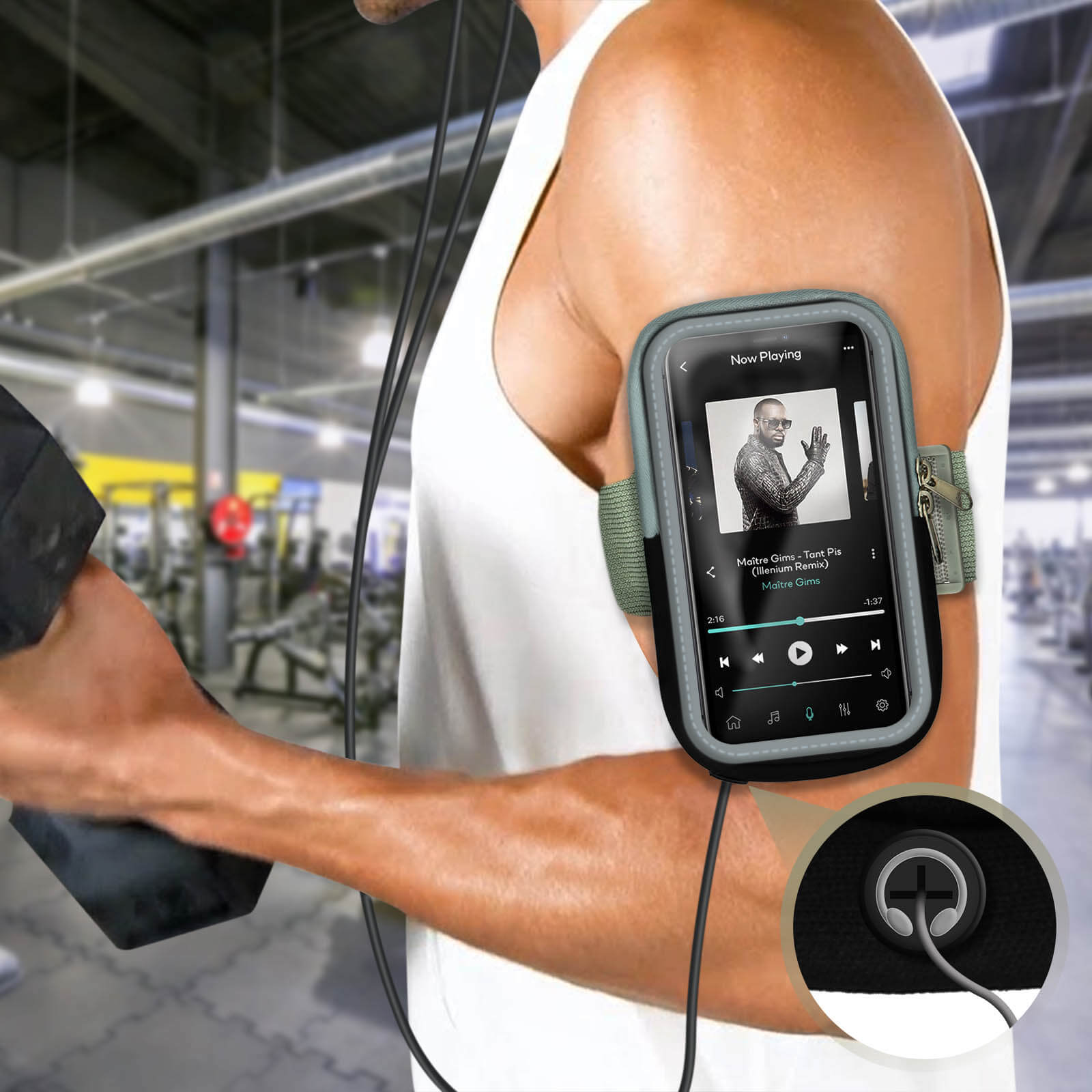 Un homme portant un débardeur blanc a un téléphone attaché à son bras. Il écoute de la musique pendant qu'il s'entraîne dans une salle de sport.