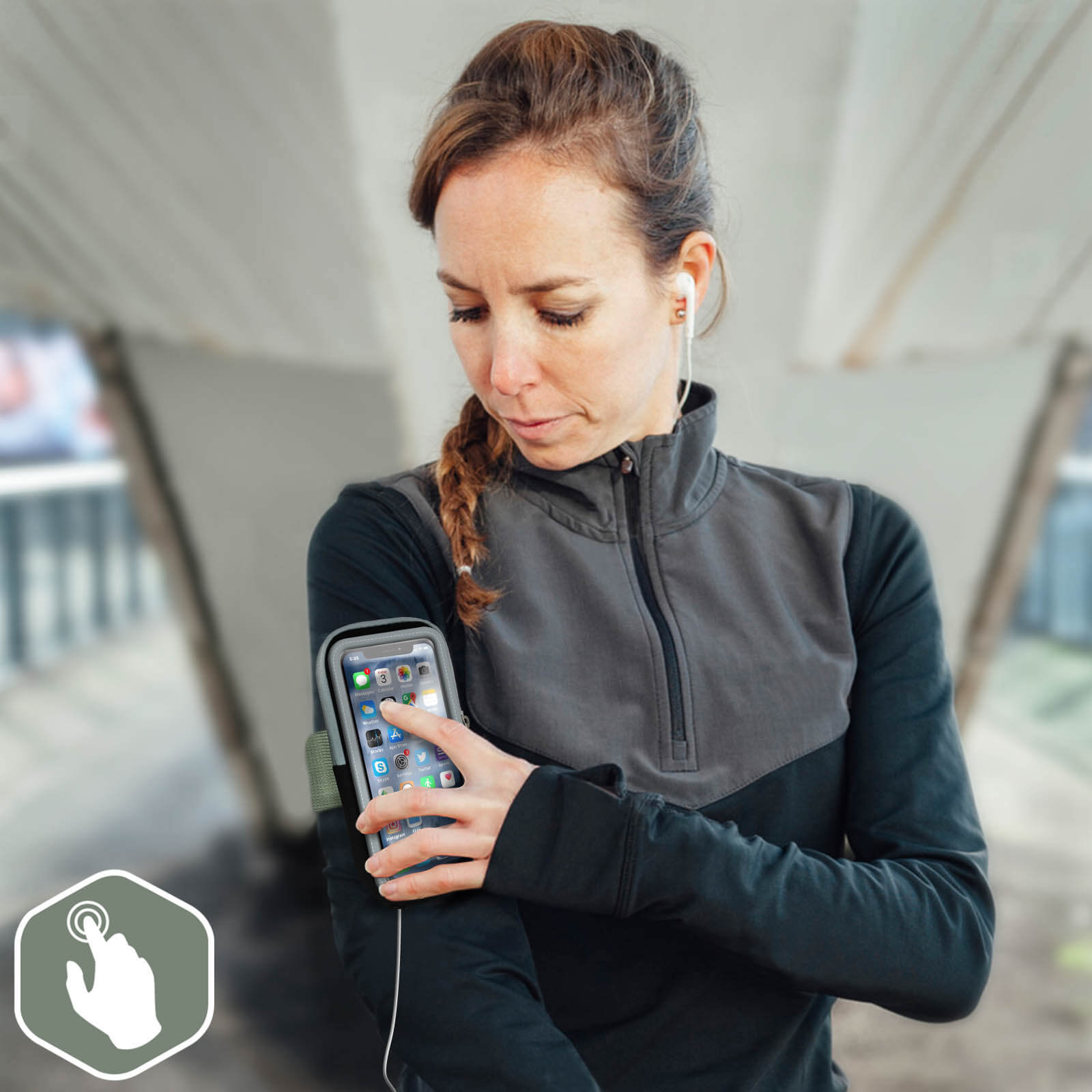 Femme en tenue de sport utilisant un smartphone dans un brassard, portant des écouteurs. En extérieur, sous une structure en forme de pont.