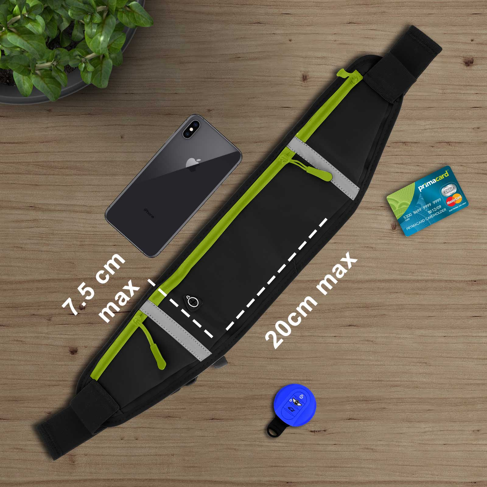 Sac banane noir avec fermeture éclair verte, iPhone, carte de crédit et clé de voiture sur surface en bois, plante.