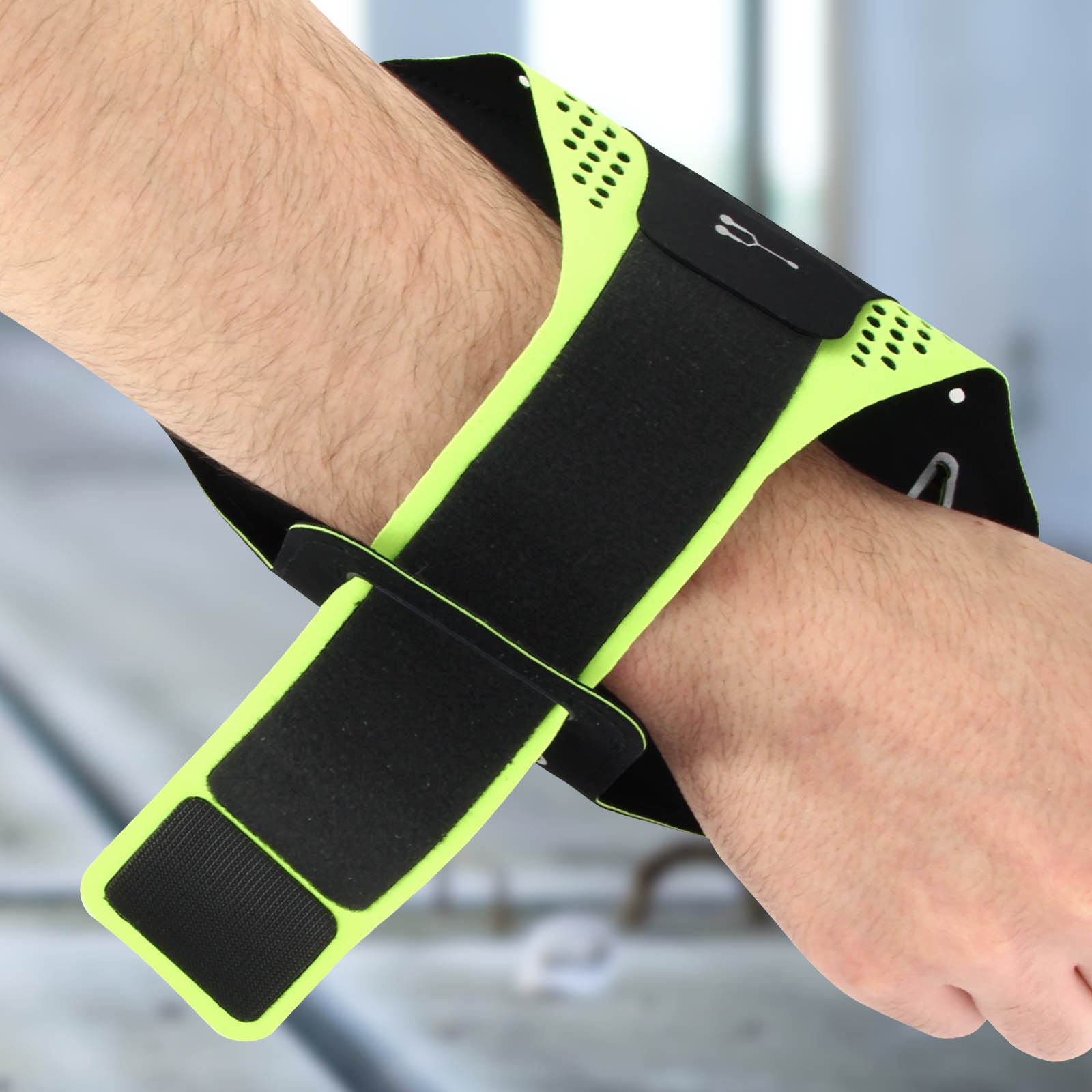 Une main avec un bracelet noir et vert est montrée. Le bracelet a du velcro et des perforations. L'arrière-plan est flou.