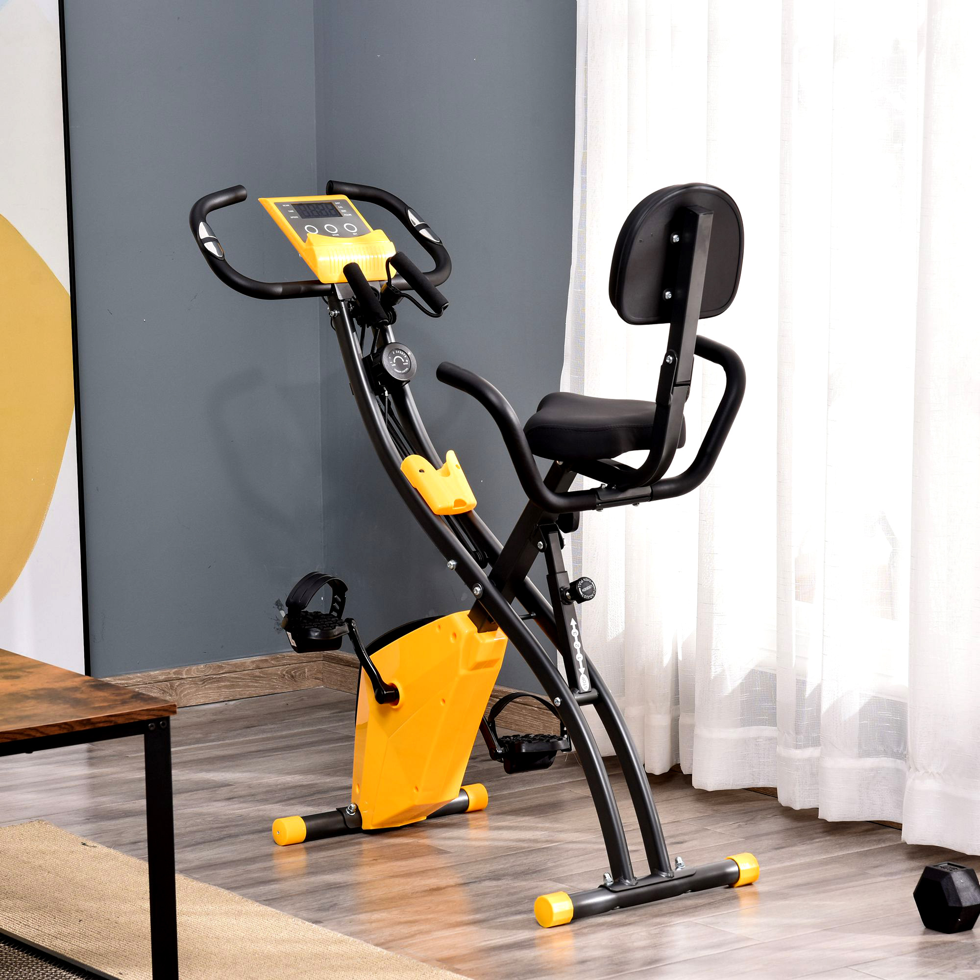 Una cyclette con telaio nero e dettagli gialli si trova su un pavimento in legno, vicino a una finestra con tende bianche.