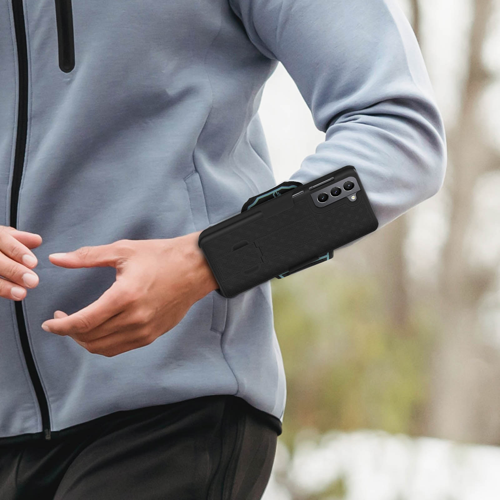 Personne portant une veste grise avec un téléphone noir attaché au bras. Arrière-plan flou, en extérieur.