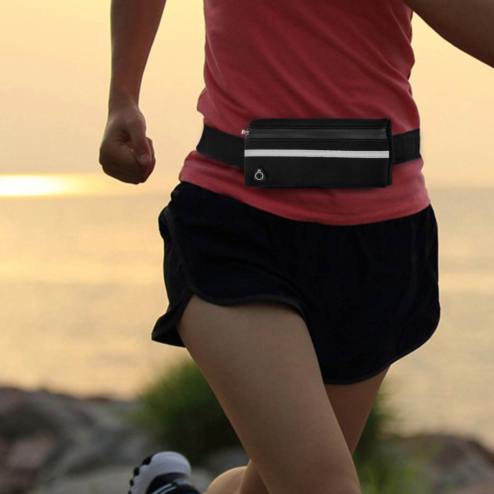Un corridore indossa un marsupio nero con una striscia bianca. Il corridore indossa una maglietta rossa e pantaloncini neri. Lo sfondo è sfocato.