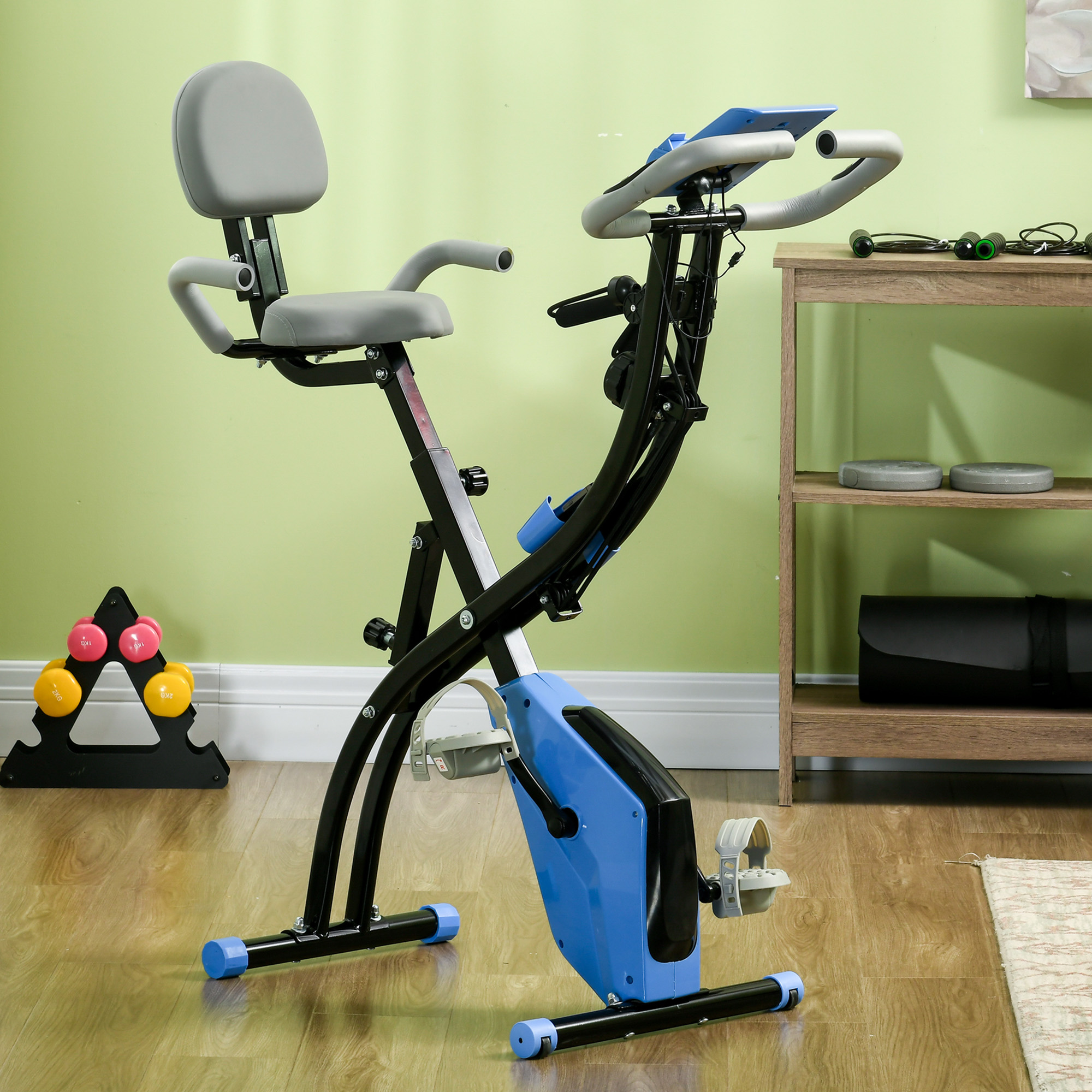 Una cyclette con telaio blu e nero, sedile grigio e manubrio. Pesi e tappetino da yoga sullo sfondo.