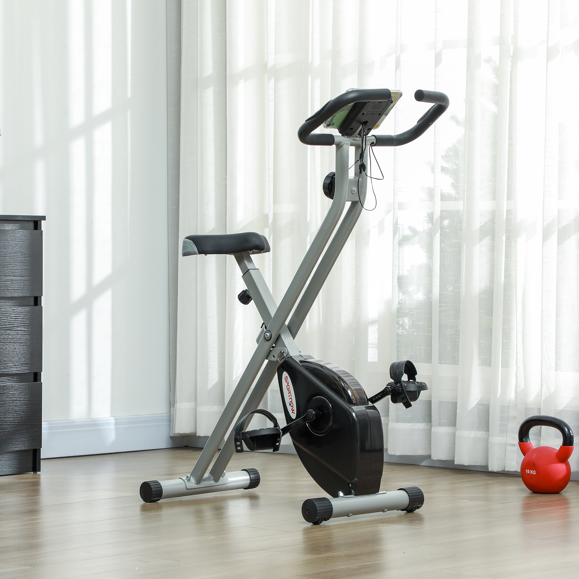Una cyclette in una stanza con finestra e tende. Un kettlebell rosso sul pavimento. Un armadio nero a sinistra.