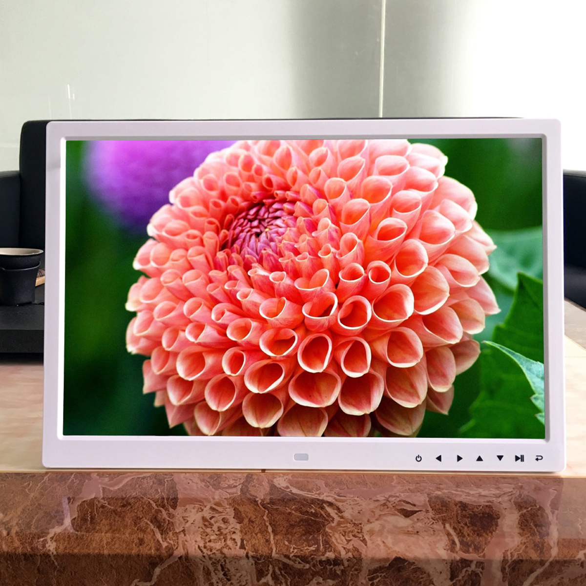 Ein digitaler Bilderrahmen zeigt eine Nahaufnahme einer korallenfarbenen Dahlie. Der Hintergrund zeigt grüne Blätter und einen Hauch von lila Blume.