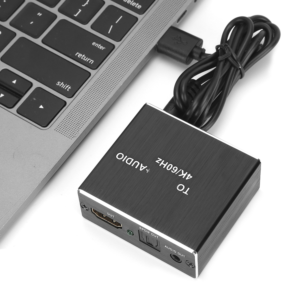 Ein schwarzer Adapter ist über USB mit einem Laptop verbunden. Der Adapter hat Anschlüsse mit der Bezeichnung 'OUT', 'SPDIF OUT' und 'AUDIO OUT'.