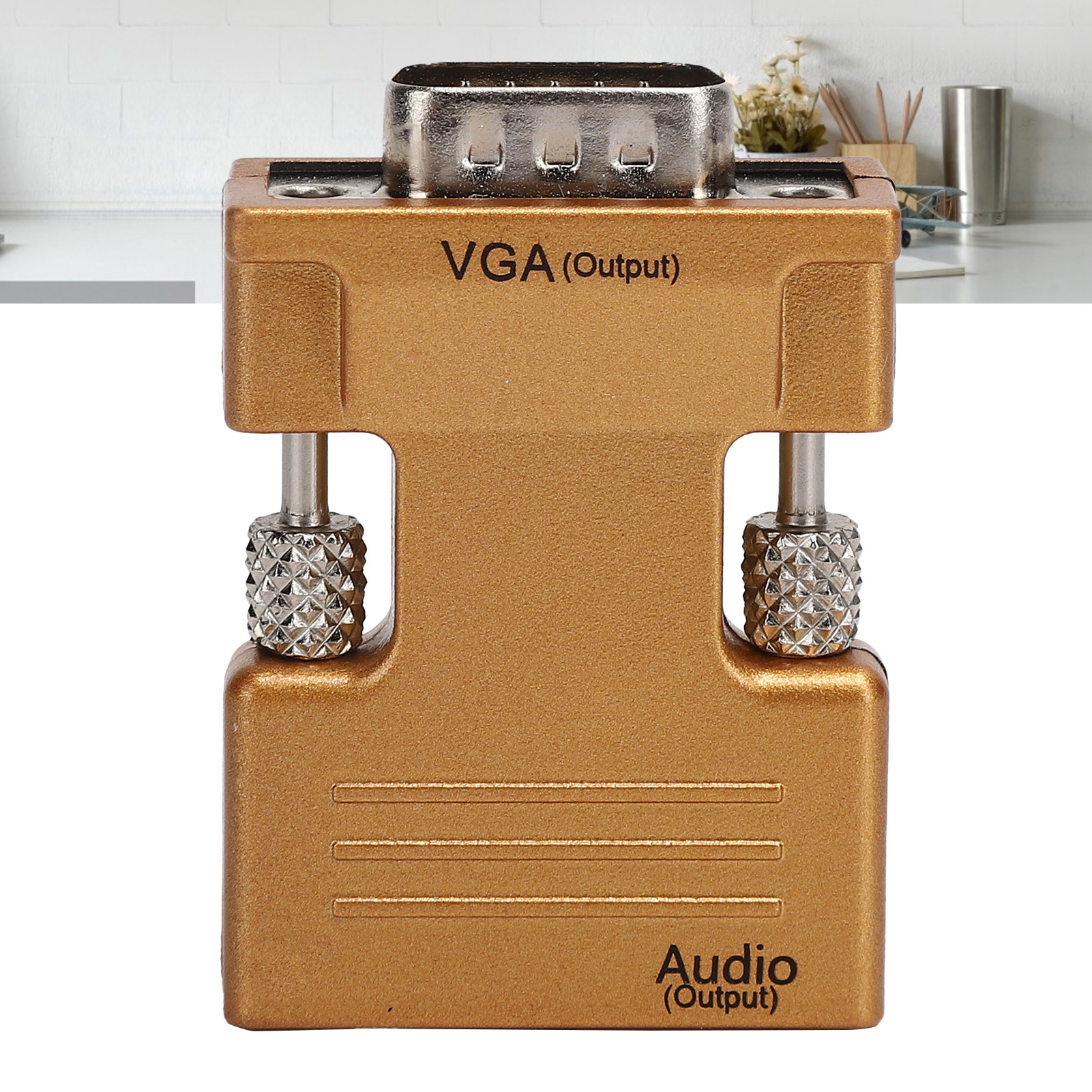 Goldener VGA-Adapter mit silbernen Anschlüssen. Text: 'VGA (Ausgang)' und 'Audio (Ausgang)'. Hintergrund: Objekte auf weißer Oberfläche.