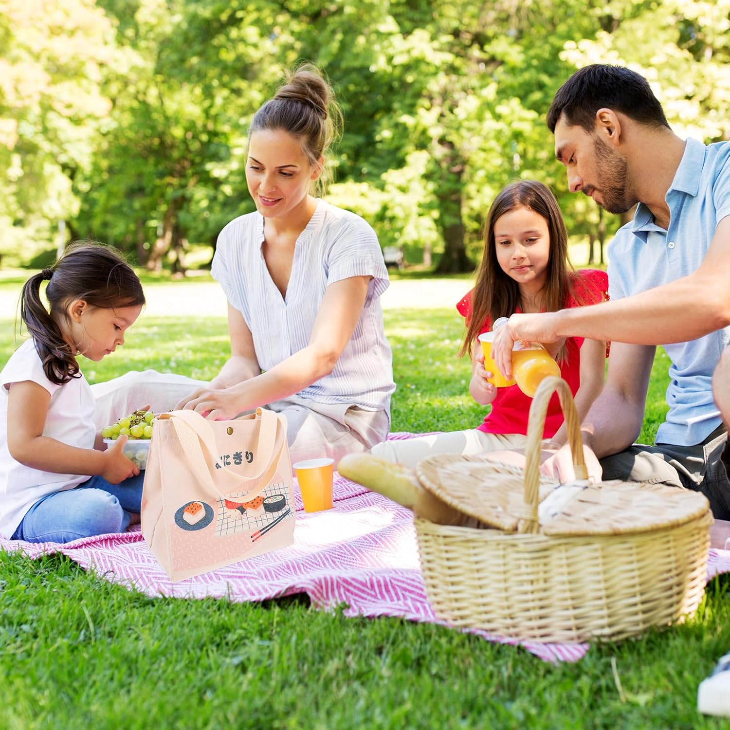 Familienpicknick auf dem Rasen. Menschen sitzen auf einer Decke. Ein Korb und eine Lunchtasche sind zu sehen.