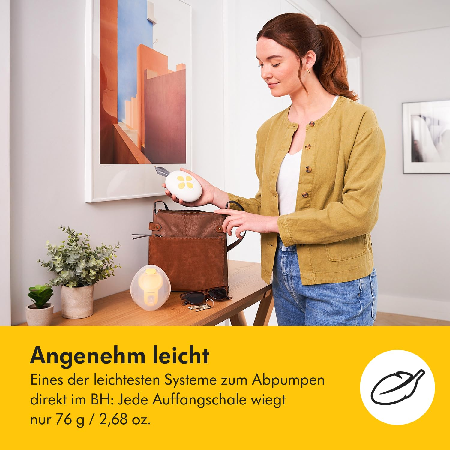 Eine Frau hält eine Brustpumpe in der Nähe eines Tisches mit einer anderen Pumpe, einer Tasche und Pflanzen. Ein Gemälde hängt an der Wand.