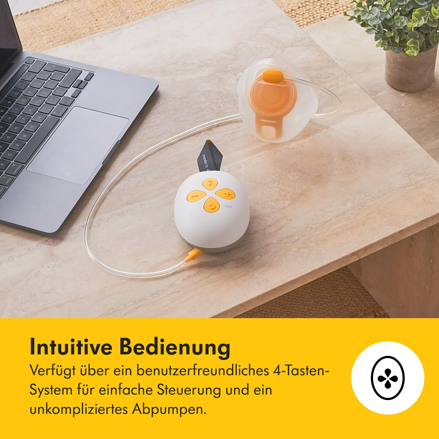 Eine Brustpumpe, ein Laptop und eine Topfpflanze auf einem Tisch. Die Pumpe ist weiß mit orangefarbenen Akzenten, der Laptop ist geöffnet.
