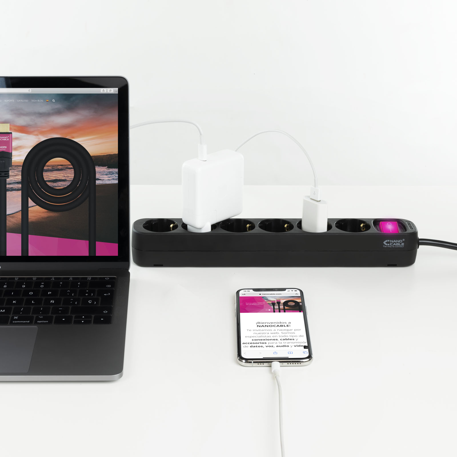 MacBook, iPhone i listwa zasilająca na białej powierzchni. Kable łączą urządzenia z zasilaczami.