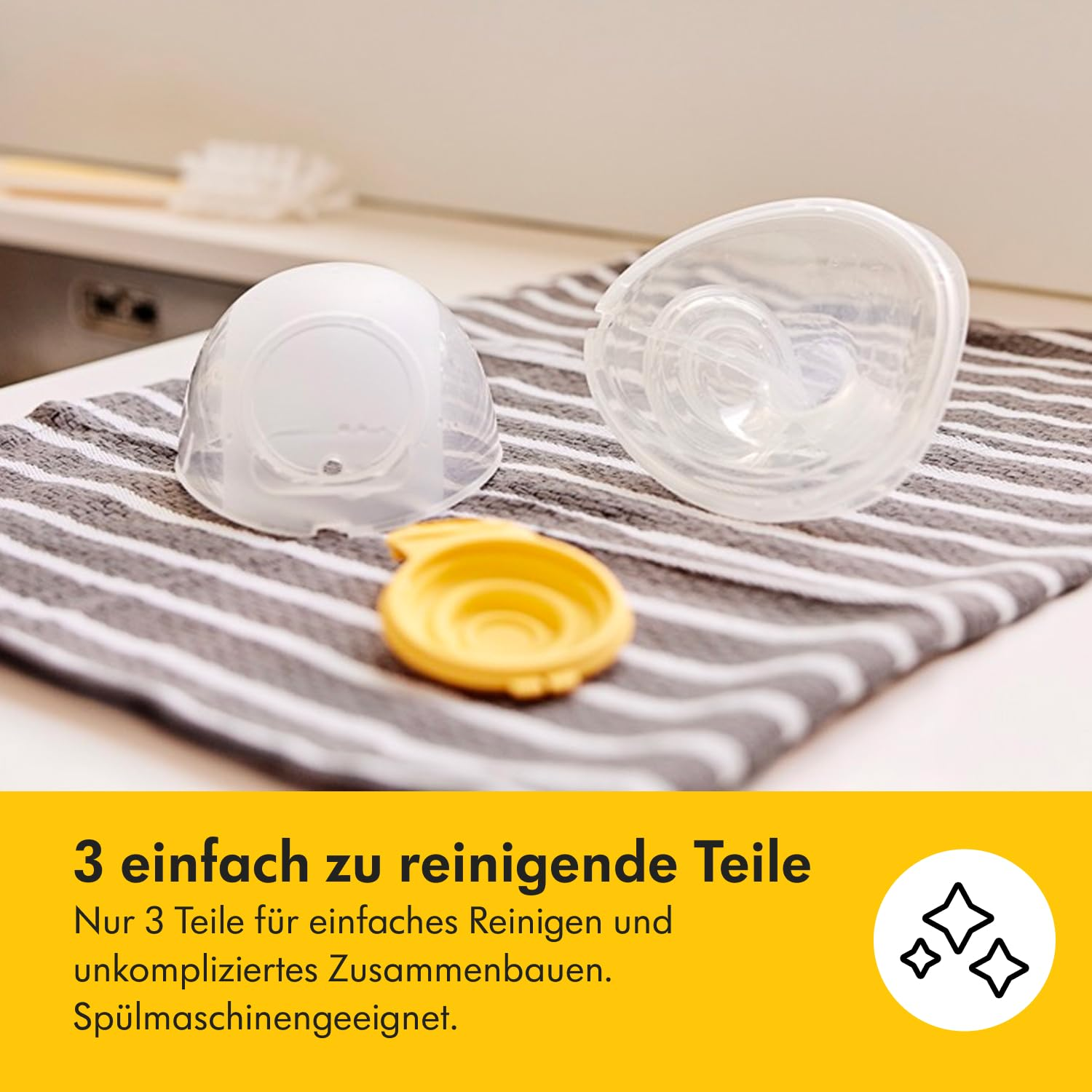 Drei klare Babyflaschenteile auf einem gestreiften Handtuch, ein gelber Deckel und zwei kuppelförmige Teile. Der Hintergrund ist eine weiße Oberfläche.