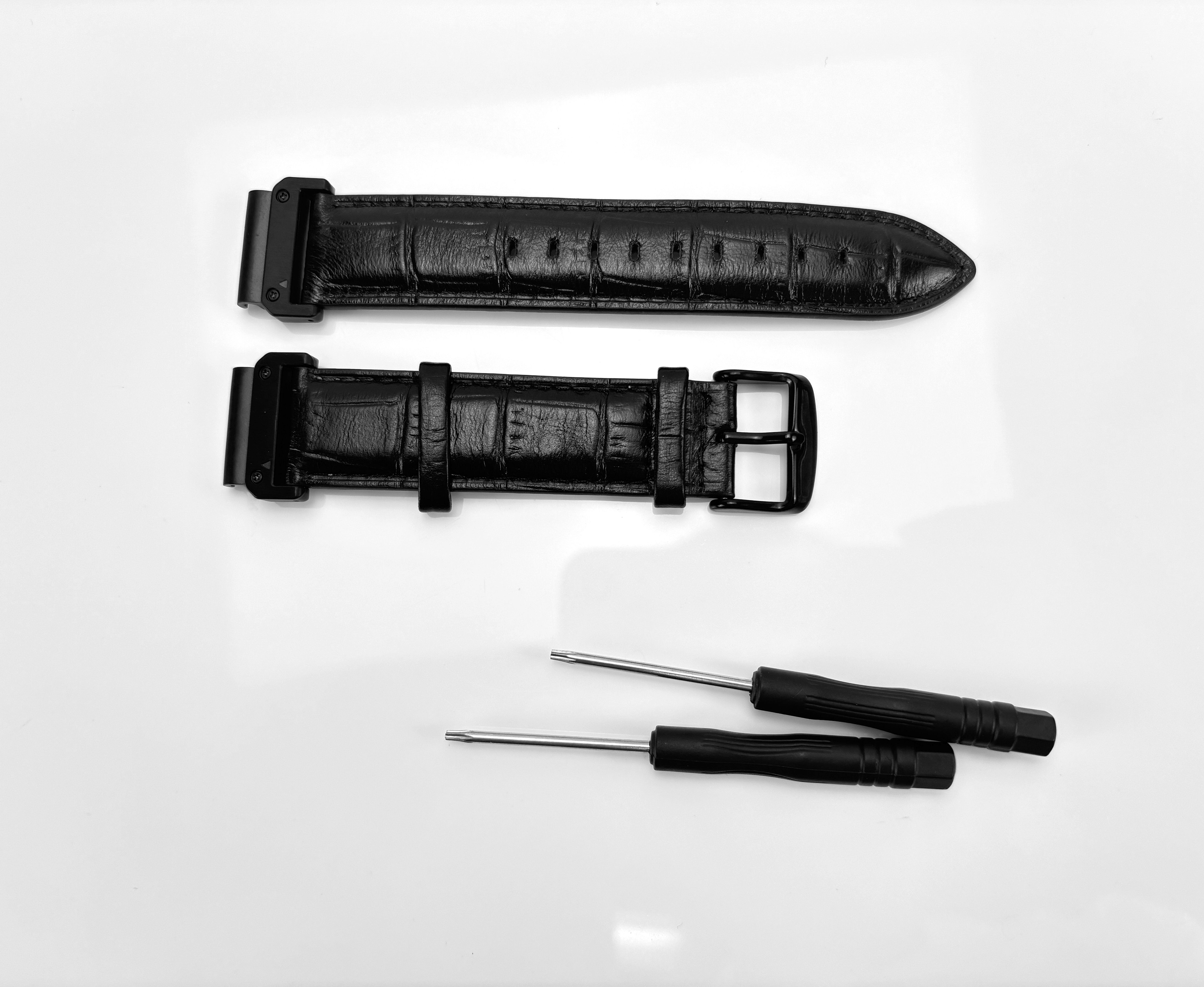 Schwarze Armbänder und zwei Schraubendreher auf weißem Untergrund. Riemen sind lederartig mit Schnallen.
