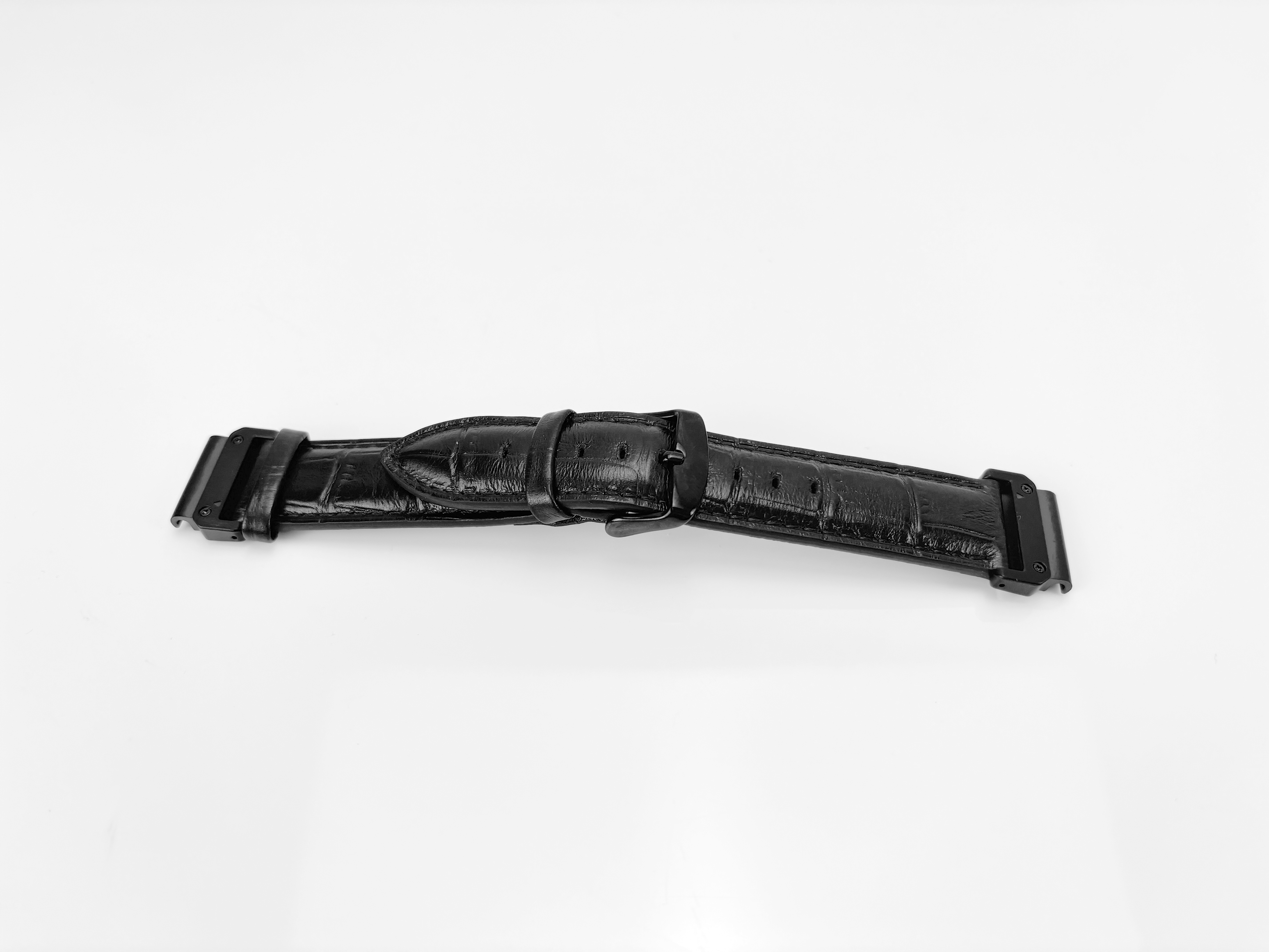 Ein schwarzes Uhrenarmband liegt auf einer weißen Oberfläche. Es ist aus Leder und hat eine Schnalle.