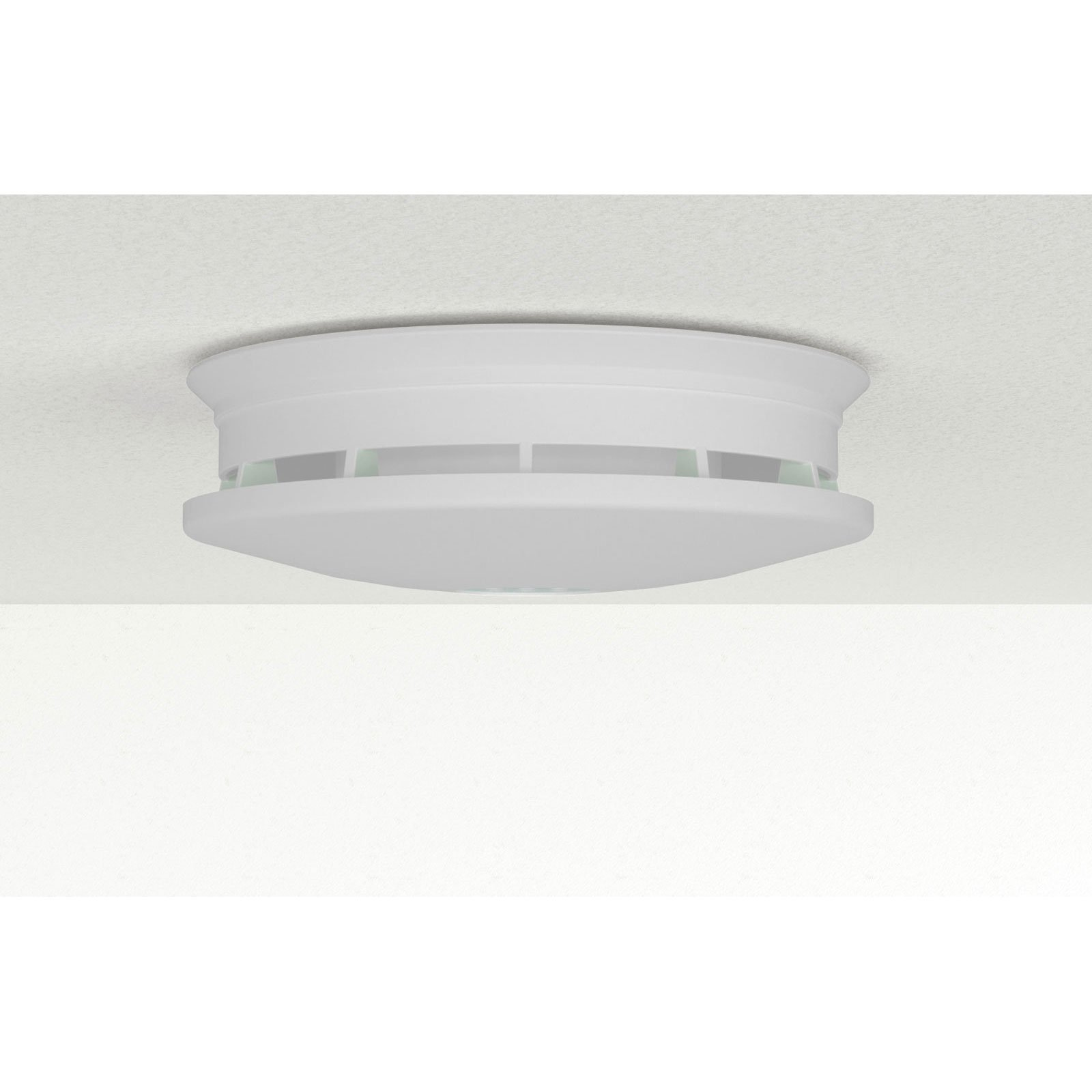 Un detector de humo blanco está montado en un techo blanco texturizado. El detector tiene un diseño redondo con una ventilación ranurada.