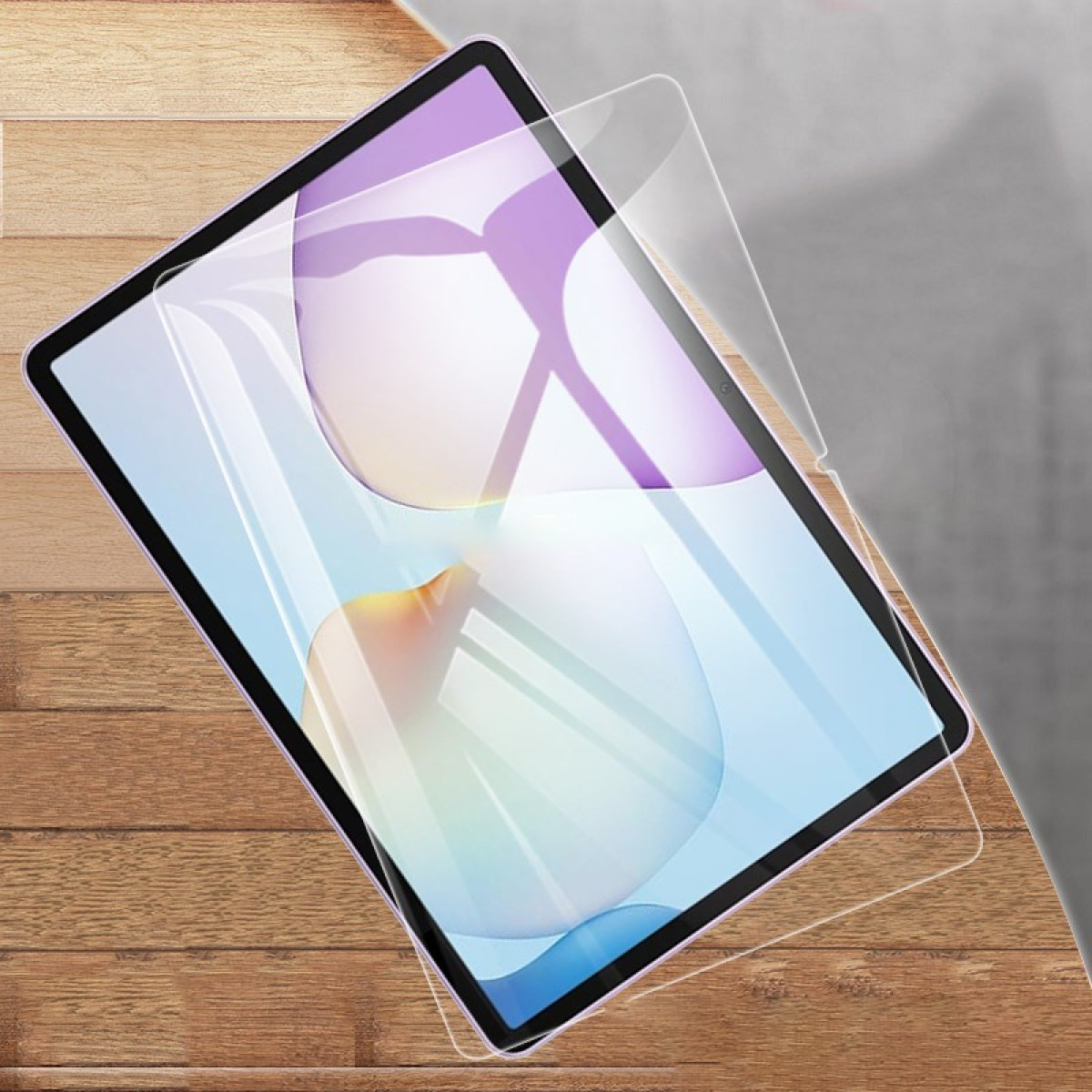 Tablet met schermbeschermer die wordt aangebracht, op houten oppervlak. Het scherm toont een kleurrijk, abstract ontwerp.