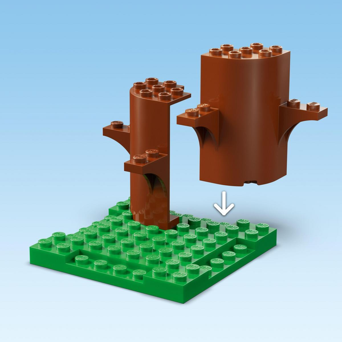 Bir Lego sahnesi. Kahverengi ağaç gövdeleri yeşil bir taban üzerine monte ediliyor. Mavi gökyüzü arka planı.