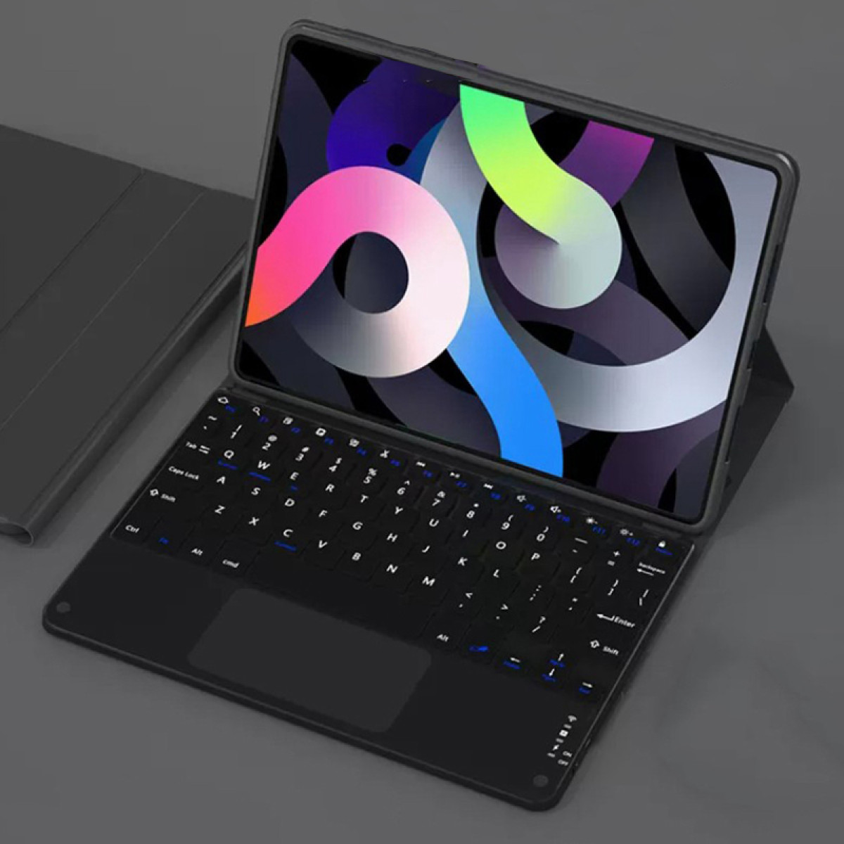 Tablet z czarną klawiaturą. Ekran wyświetla kolorowy abstrakcyjny wzór. Klawiatura jest podłączona i na szarej powierzchni.