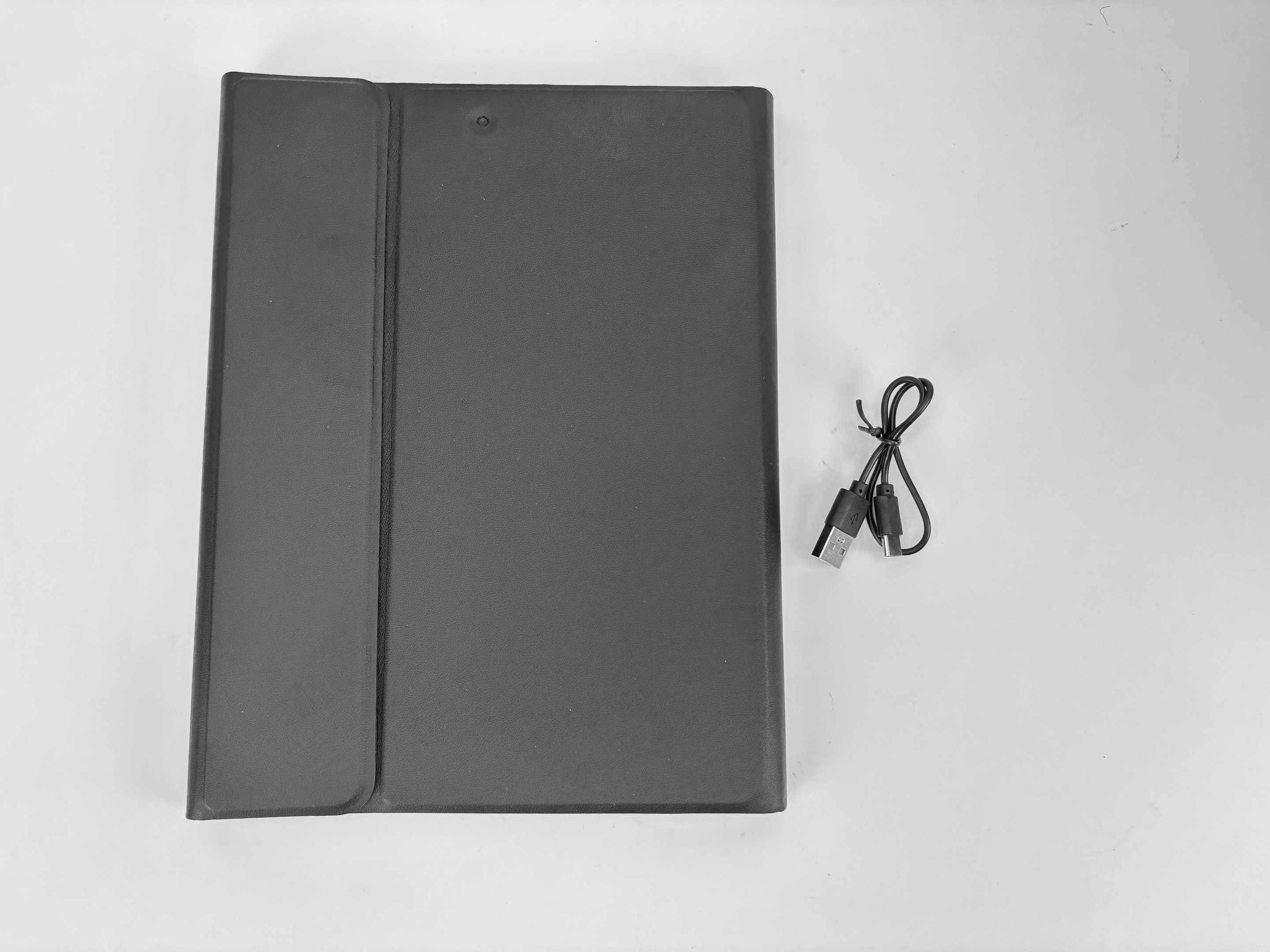 Una custodia nera per tablet aperta su una superficie bianca, con un cavo di ricarica a destra.