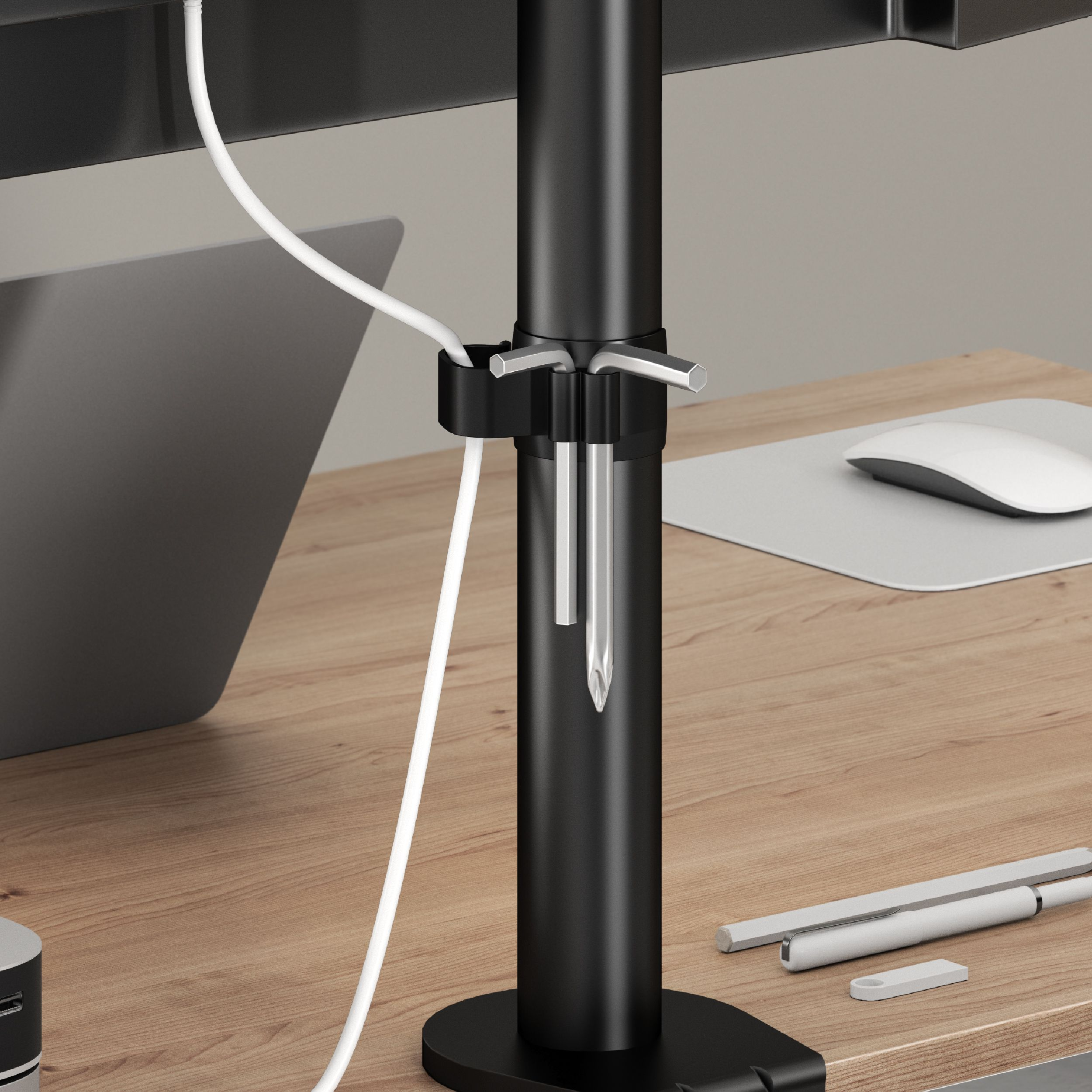 Un soporte de monitor negro sostiene herramientas y un cable blanco. Un ratón, una alfombrilla y accesorios de escritorio están sobre un escritorio de madera.
