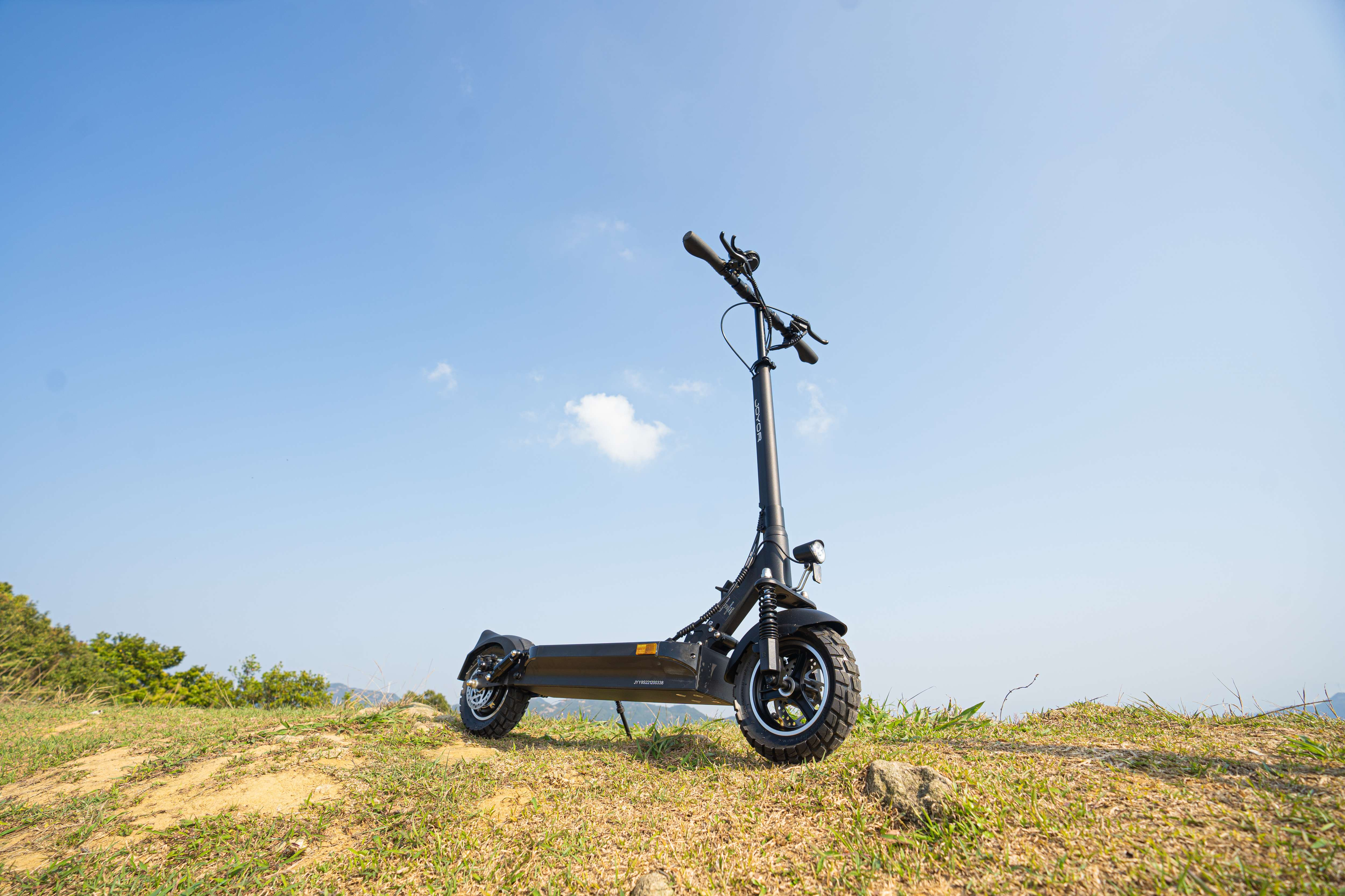 Czarna hulajnoga elektryczna na trawiastym wzgórzu, tle błękitnego nieba. Hulajnoga ostra, z wyraźnym tłem.