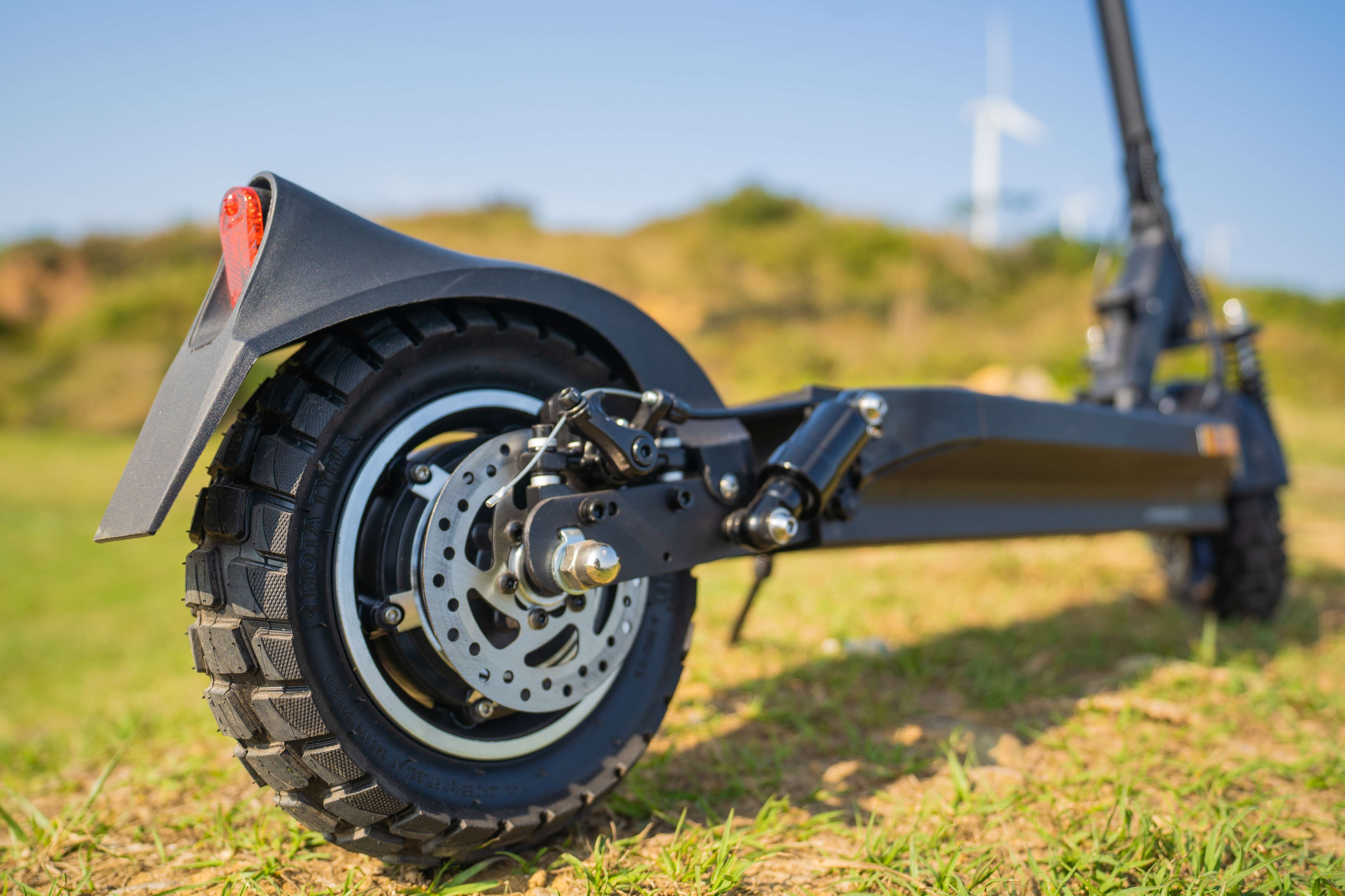 Czarny skuter elektryczny na trawie, szczegół tylnego koła. Jasne, błękitne niebo w tle.