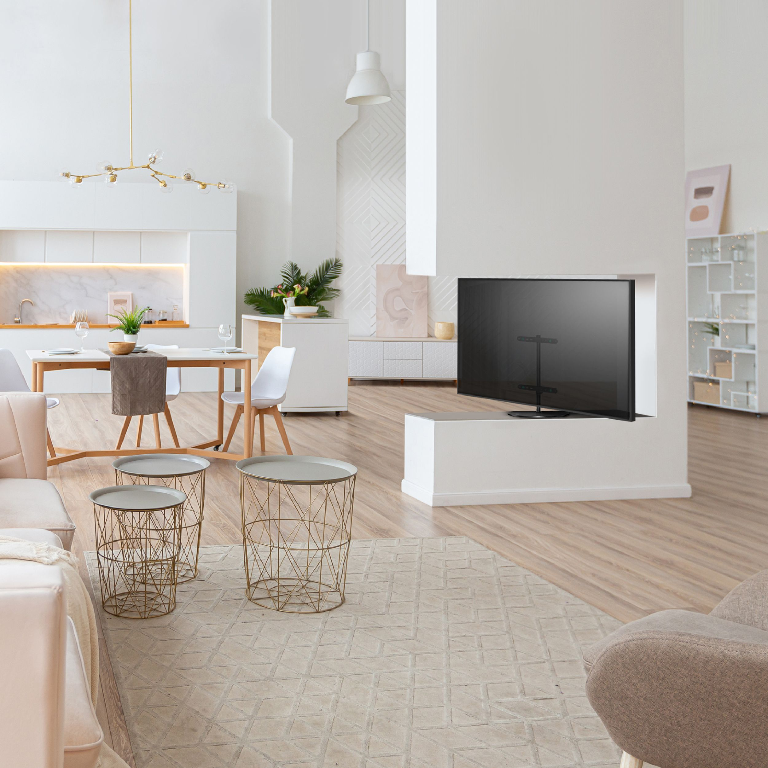 Ein moderner Wohnraum mit Essbereich, großem TV, goldenen Beistelltischen und beigem Teppich. Die Wände sind weiß.
