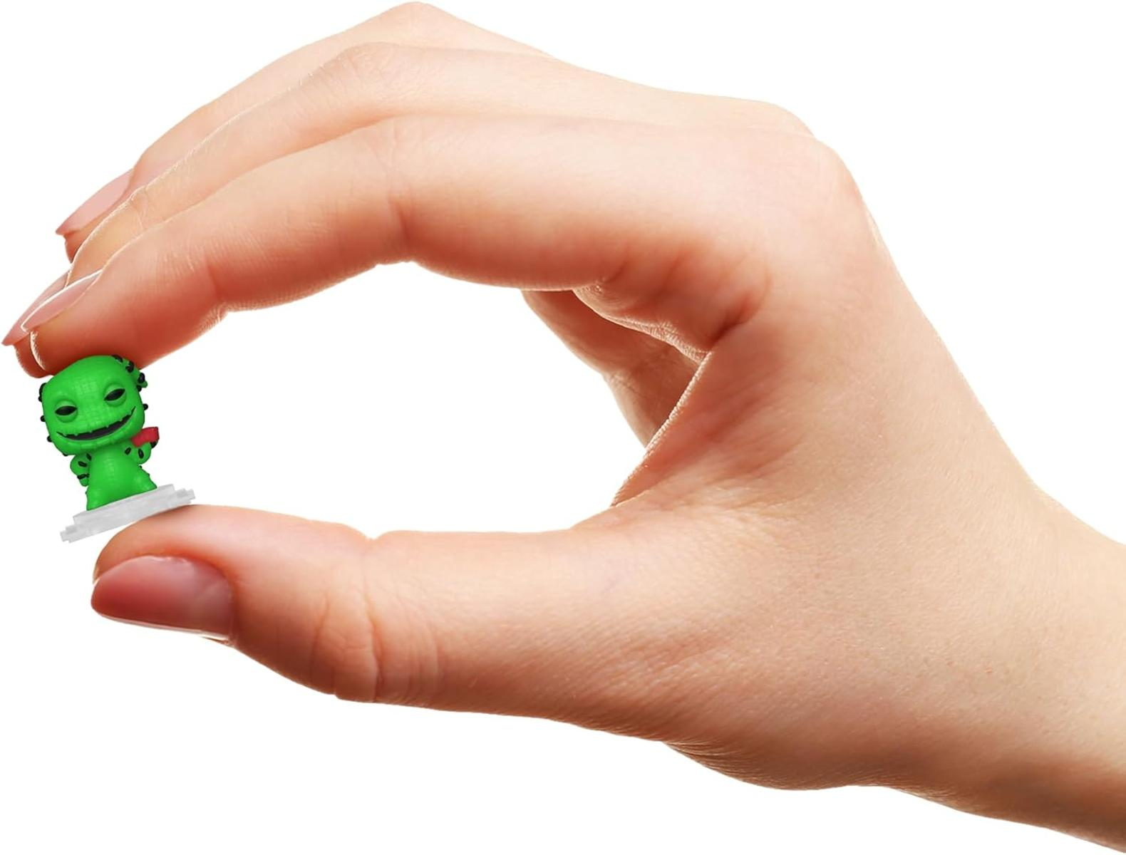 Una mano tiene una piccola figura verde, simile a una lucertola. La figura è su una base bianca. Lo sfondo è bianco.