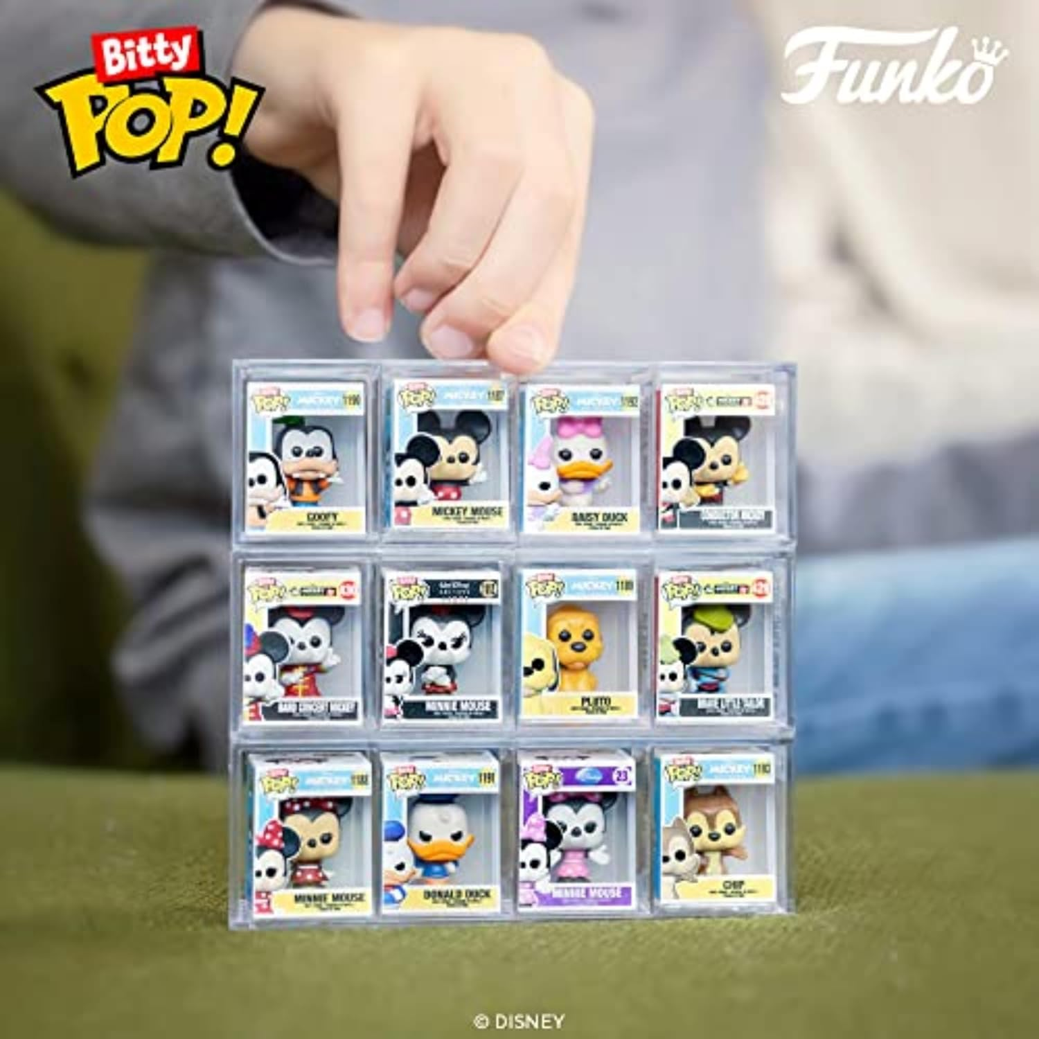 Dłoń trzyma wieżę figurek Funko Pop w przezroczystych etui. Postacie to Myszka Miki, Myszka Minnie, Kaczor Donald, Kaczka Daisy i Goofy.