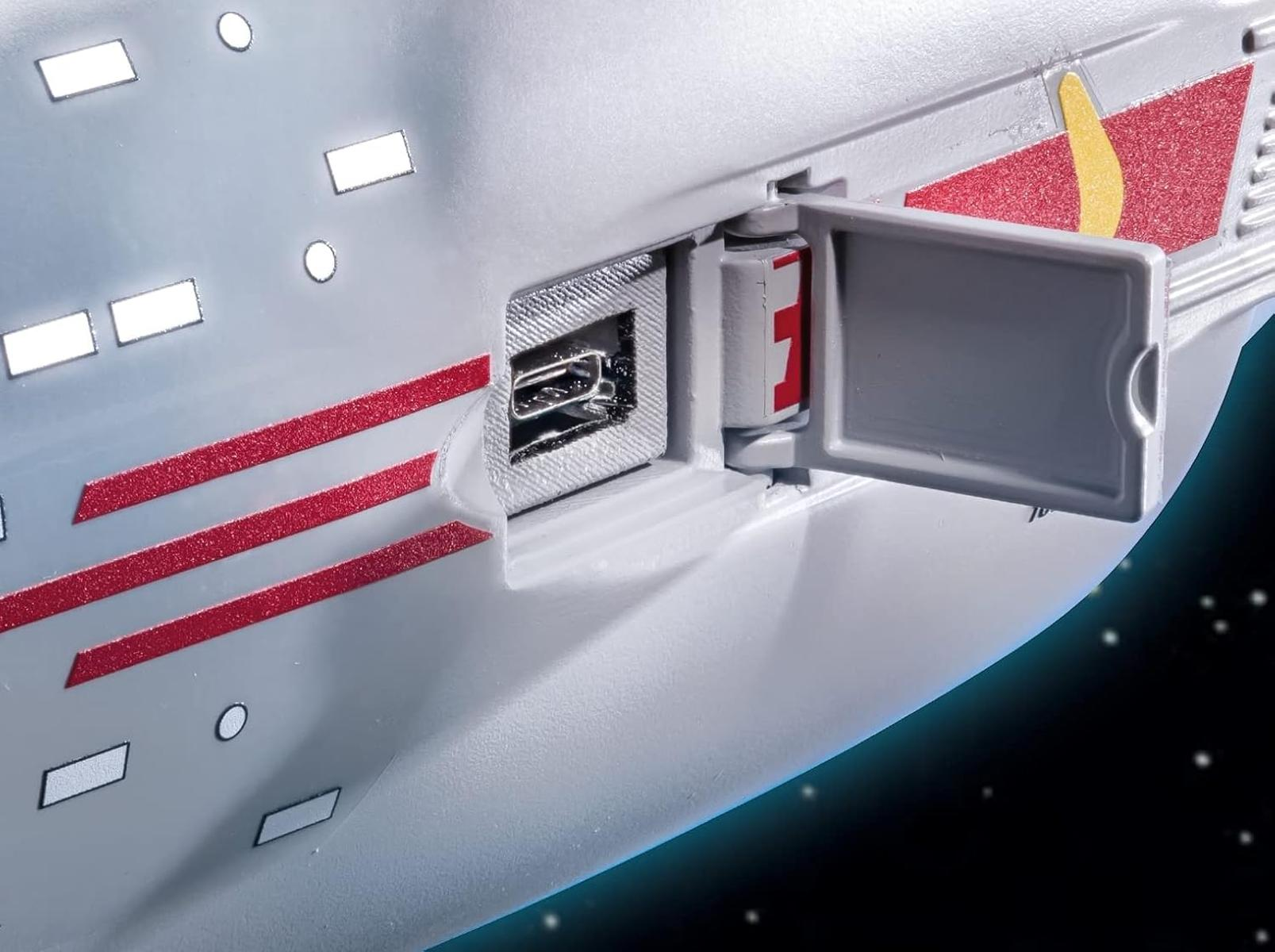 Primo piano di un'astronave bianca con strisce rosse e una porta aperta che rivela una porta USB e un oggetto rosso.